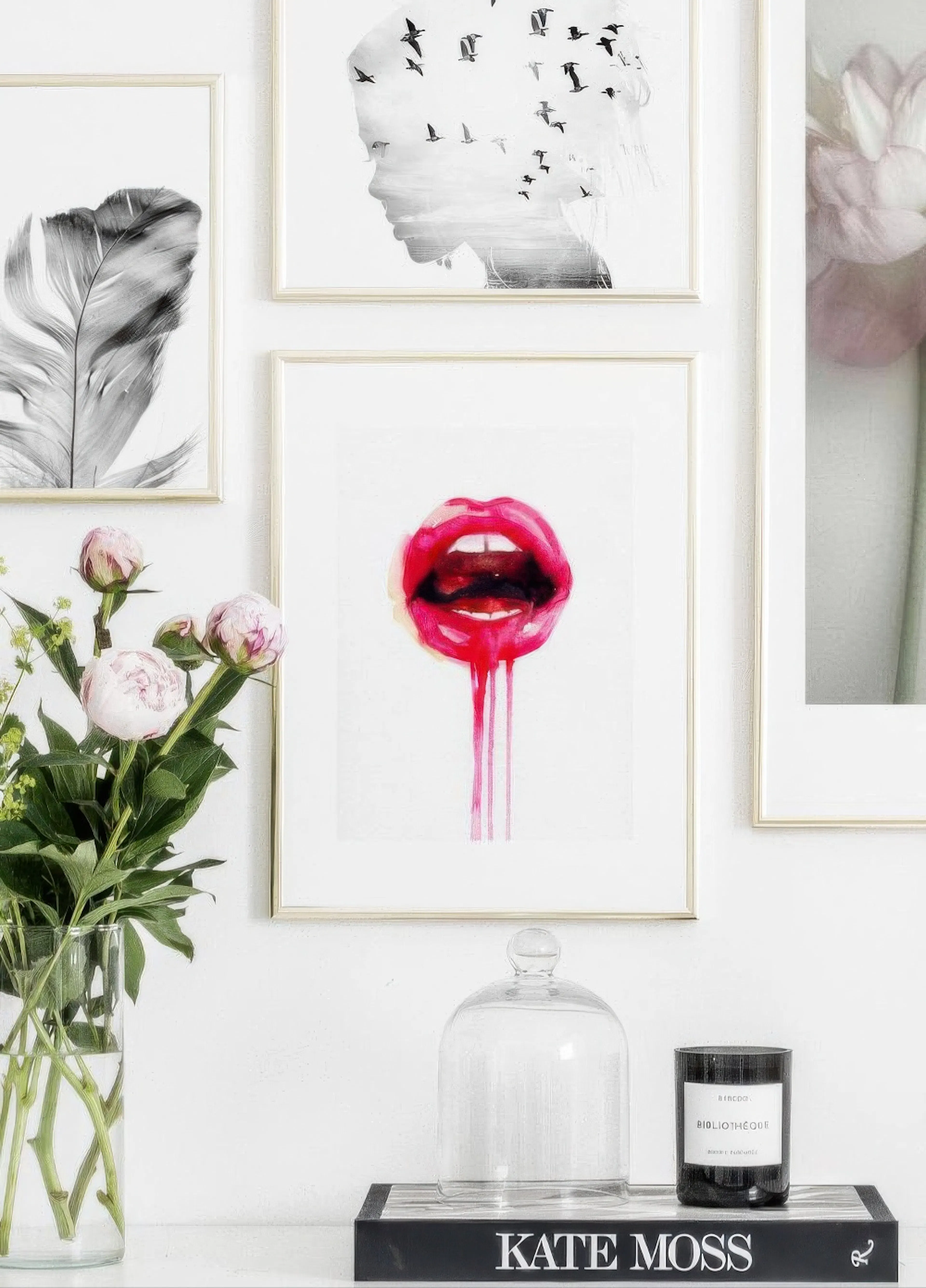 A vibrant red dripping lips poster, part of a gallery wall, next to a vase of peonies and a book on a shelf.