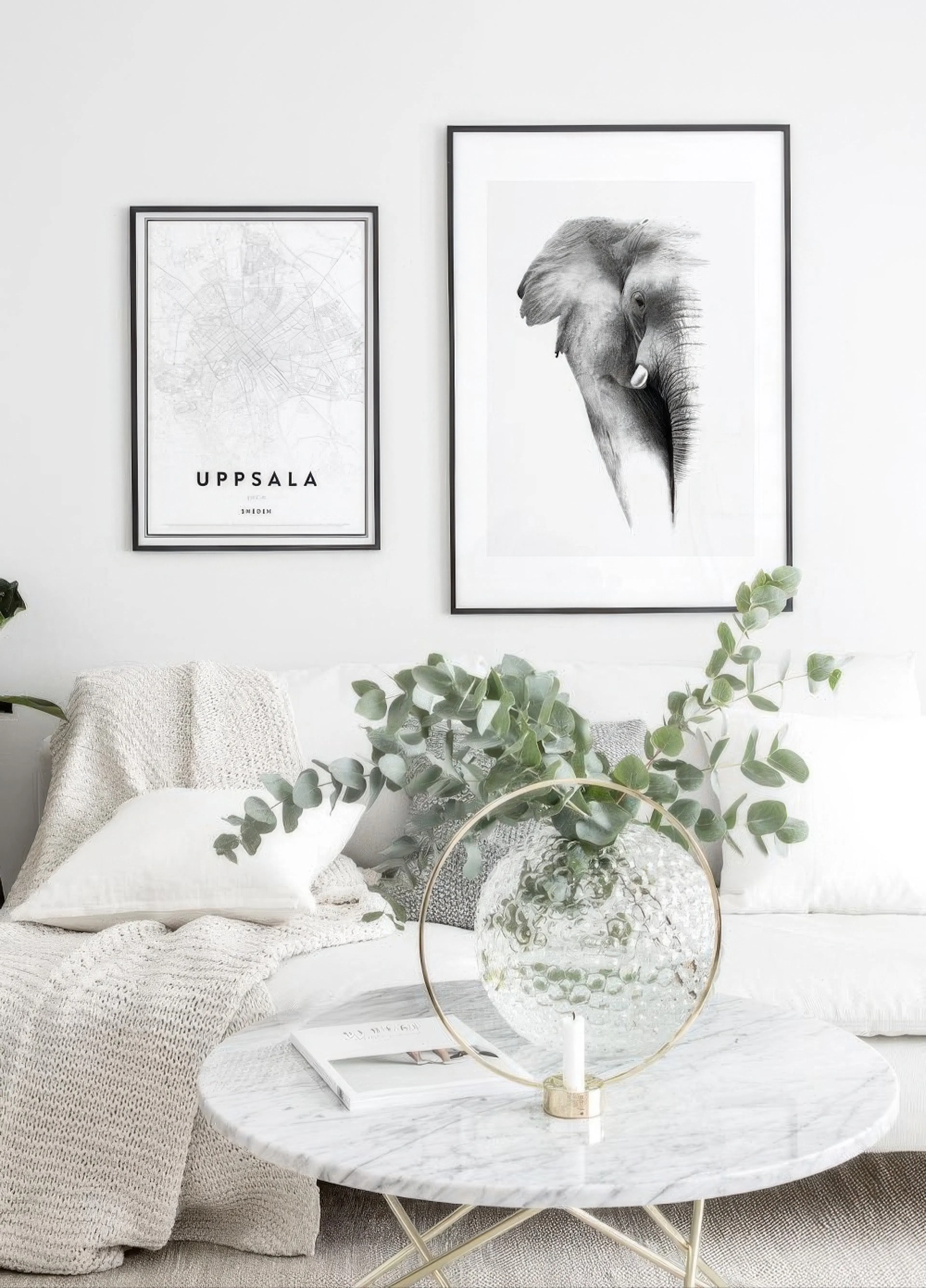Black and white poster of an elephant head and a map of Uppsala, Sweden, hanging above a white couch in a living room.