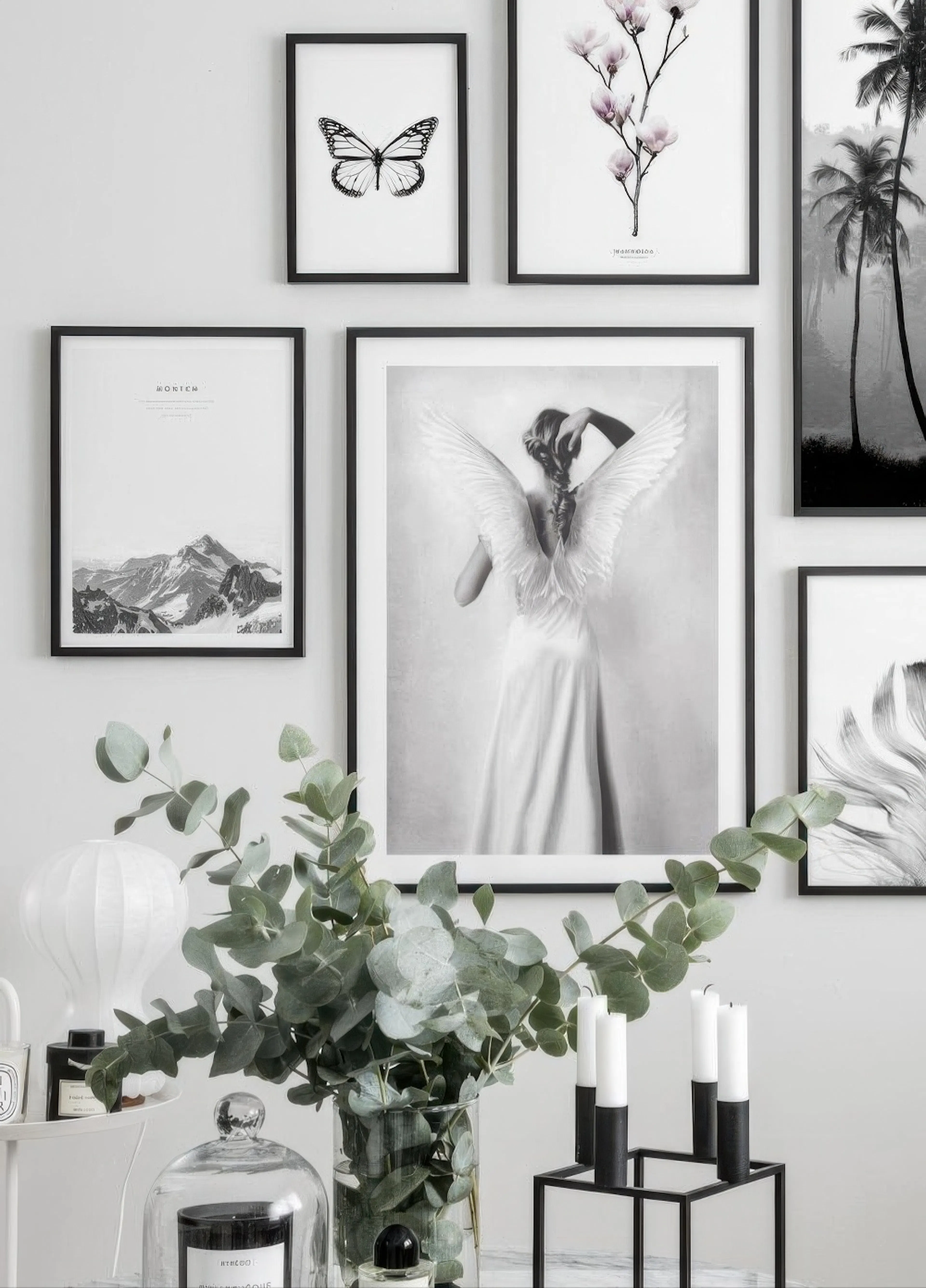 A gallery wall featuring a black and white poster of a woman with angel wings, alongside posters of a butterfly, magnolia flower