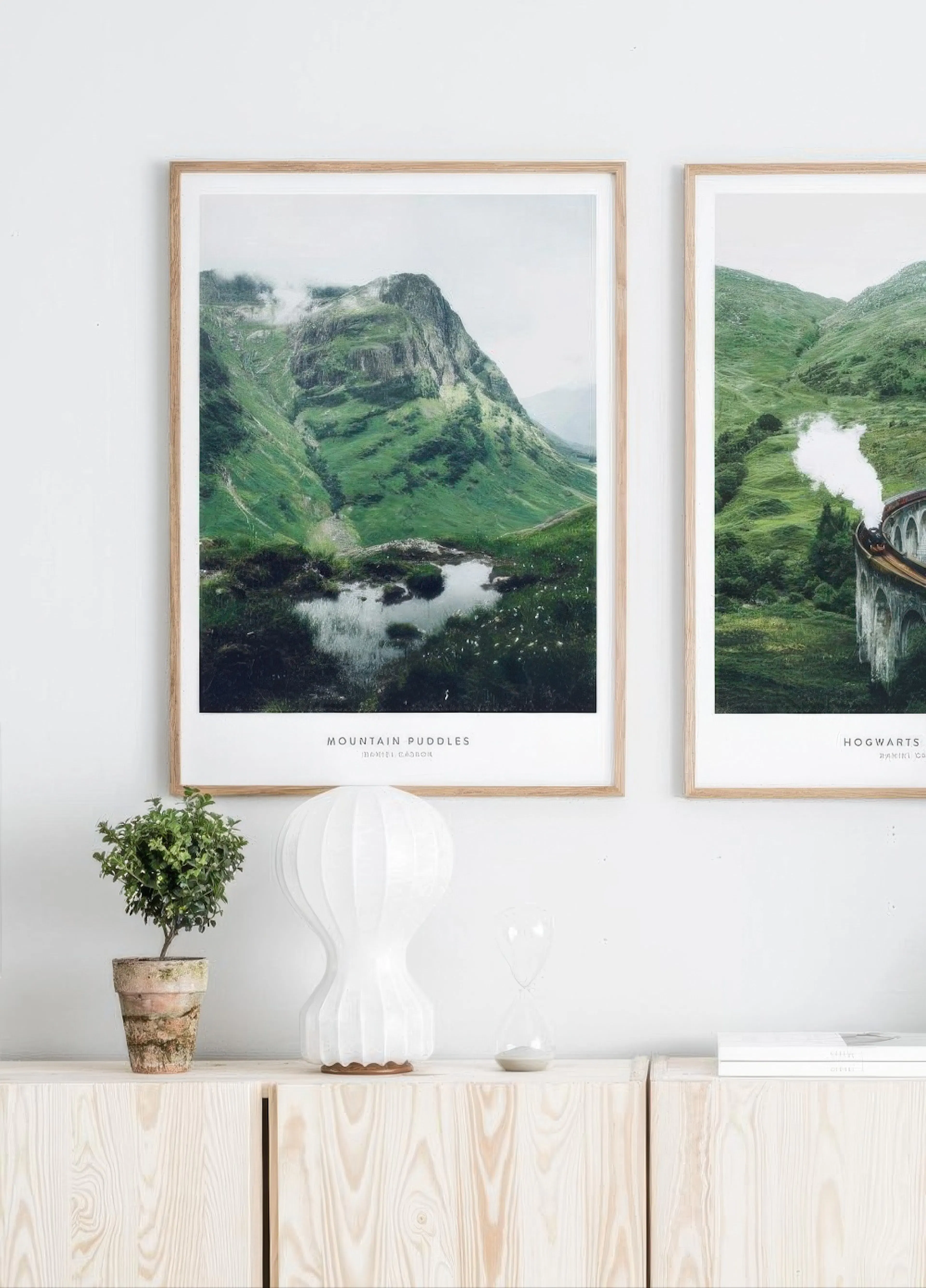 Poster of a green mountain with misty clouds and a small pond, displayed on a gallery wall above a light timber cabinet.