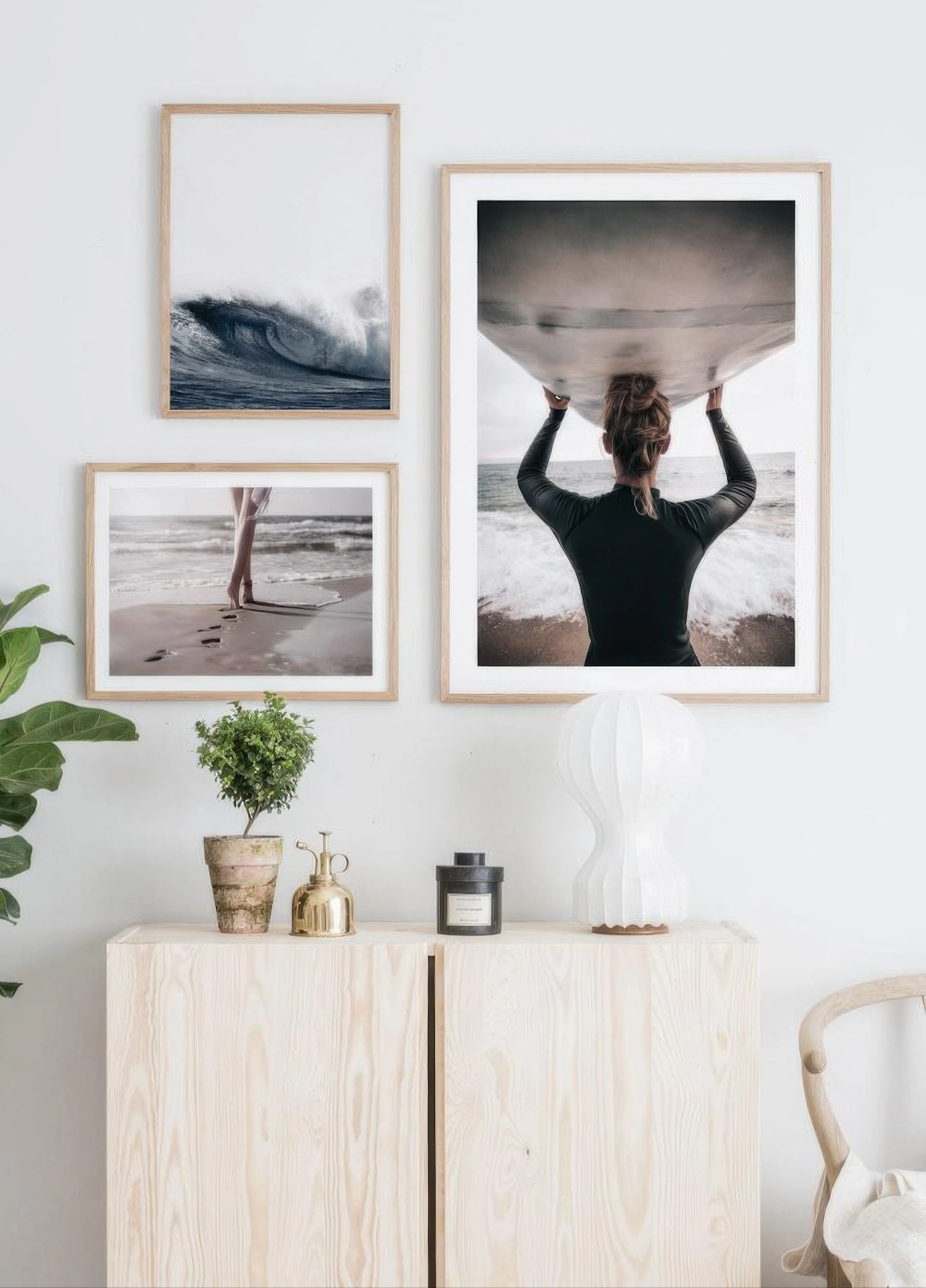 A gallery wall with three surf-themed posters above a light wooden cabinet with plants and decor.