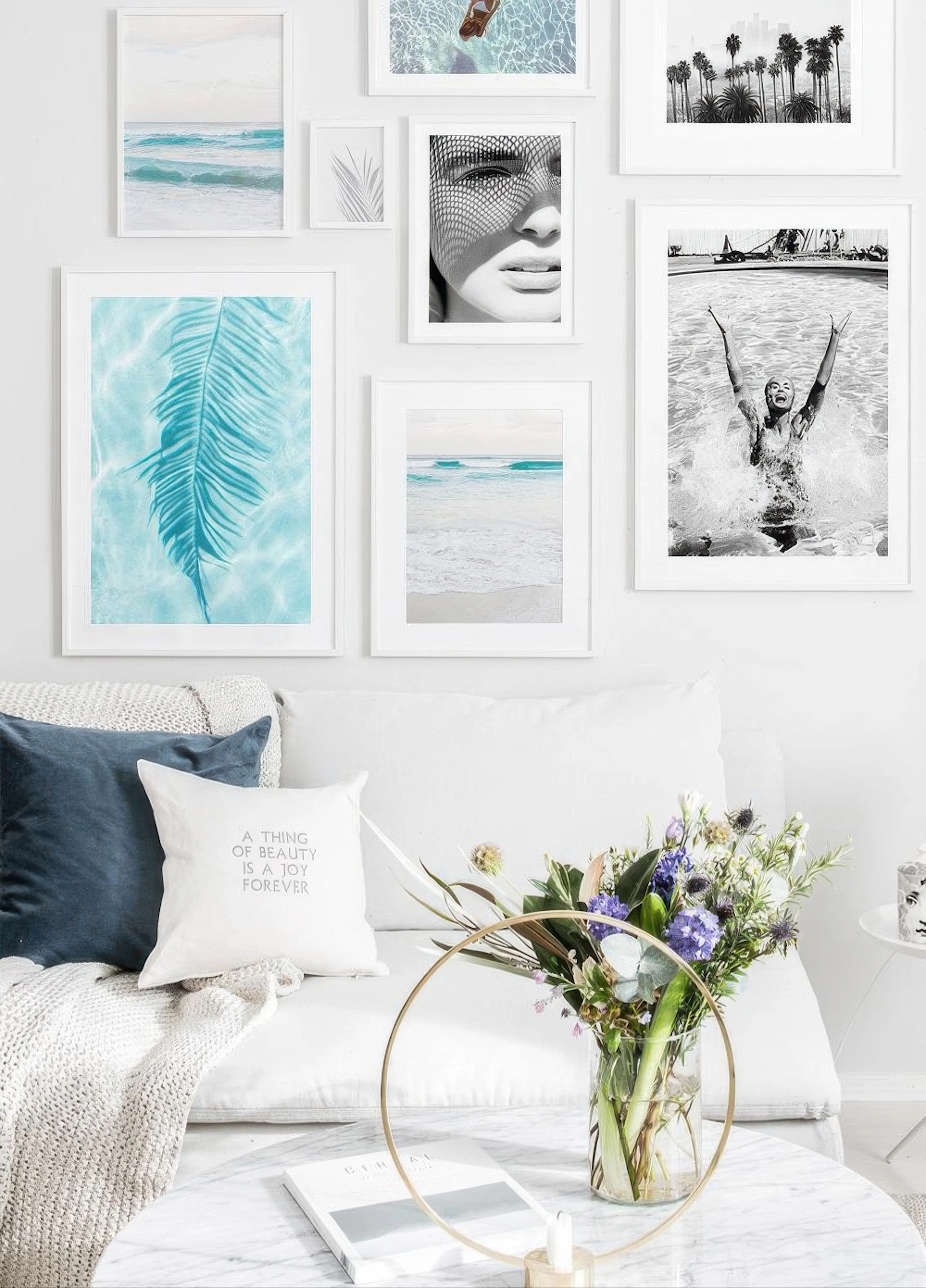 A gallery wall of coastal and black and white prints, including a tropical leaf and ocean waves, displayed above a white sofa.