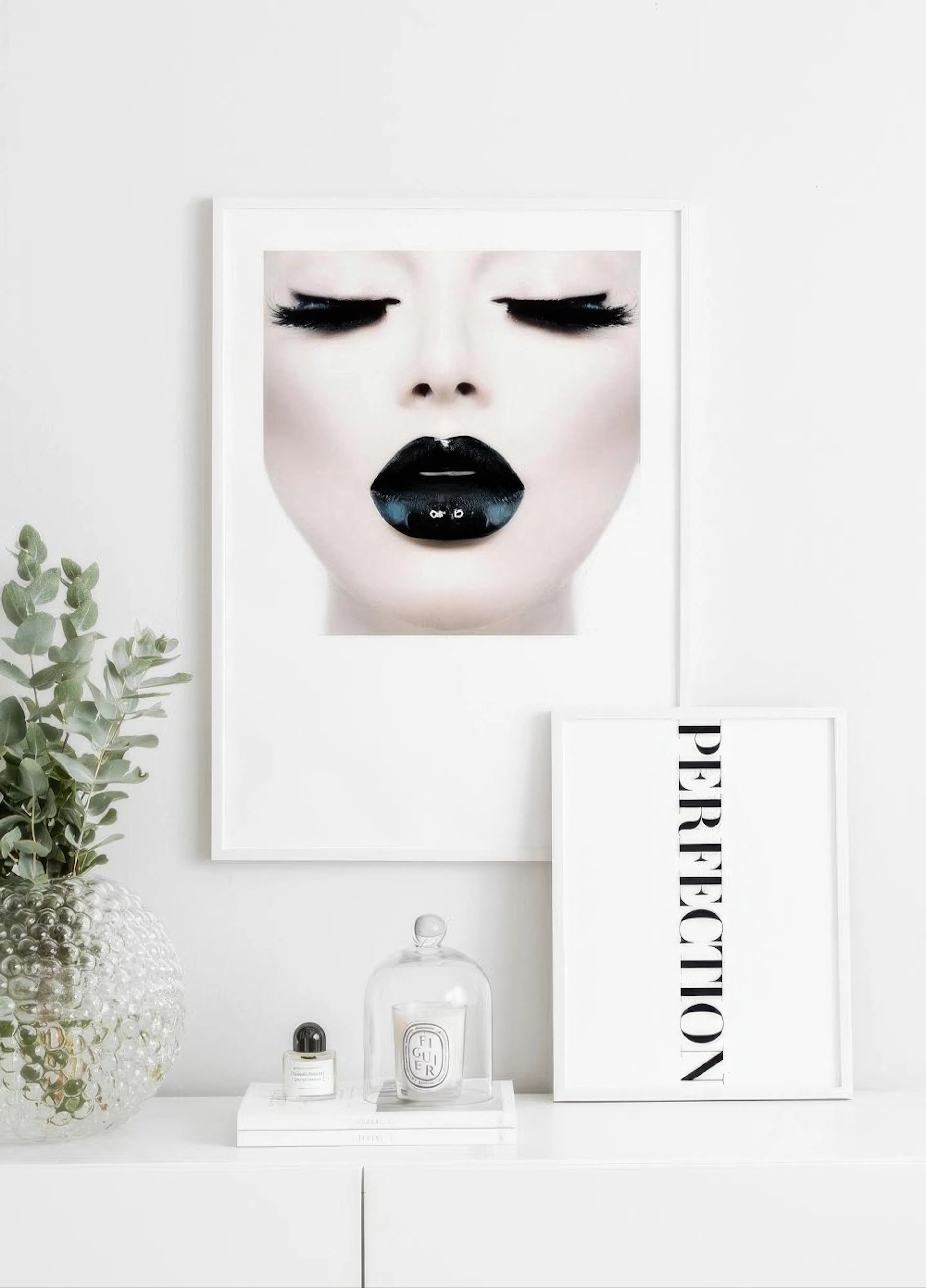 A poster of a womans face with closed eyes, long black lashes, and glossy black lips, displayed on a white wall in a modern room