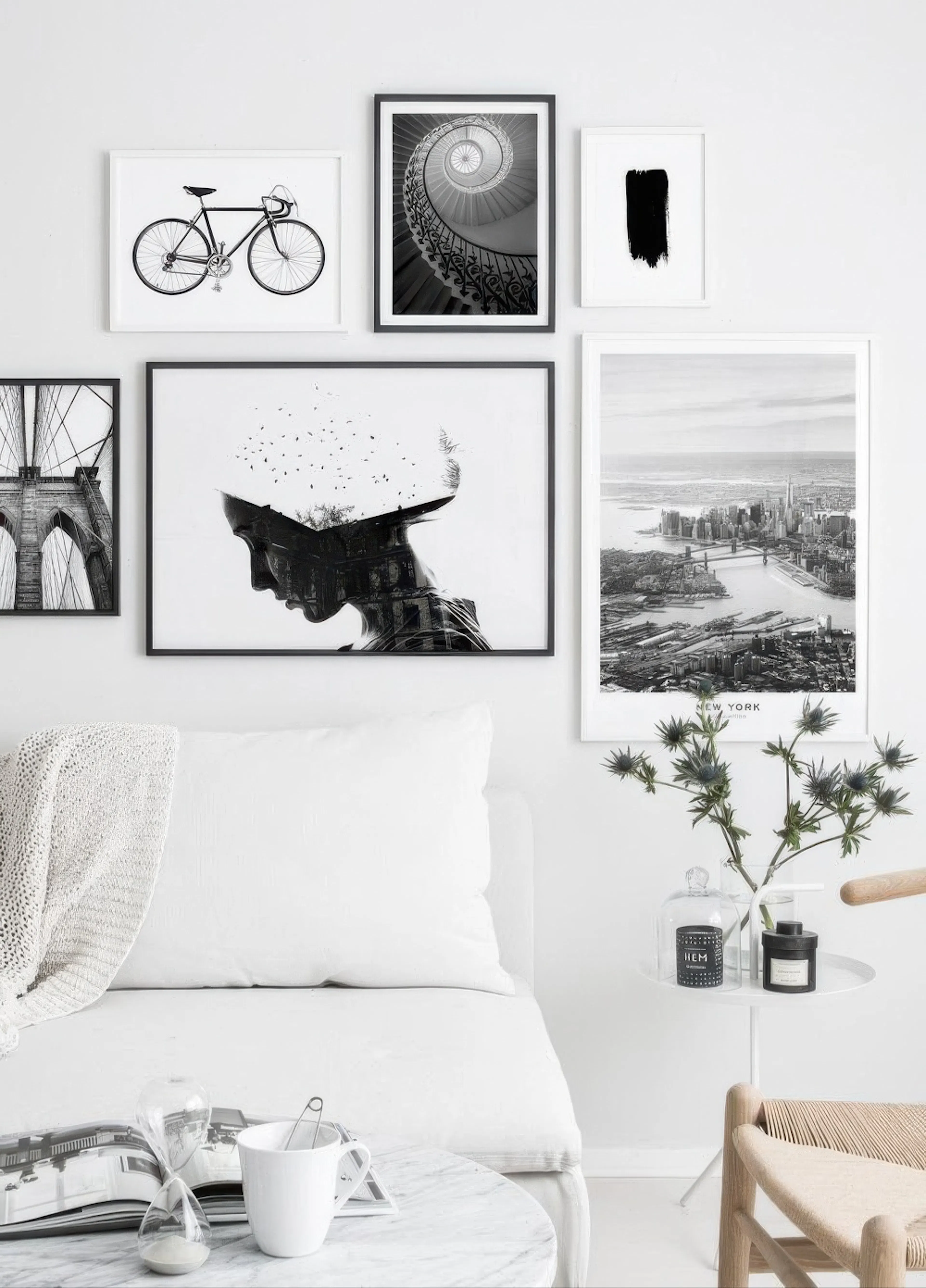 Mustavalkoinen tauluseinä valkoisessa olohuoneessa, jossa on sohva ja marmoripöytä. Julisteet esittävät polkupyörää, kierreporta