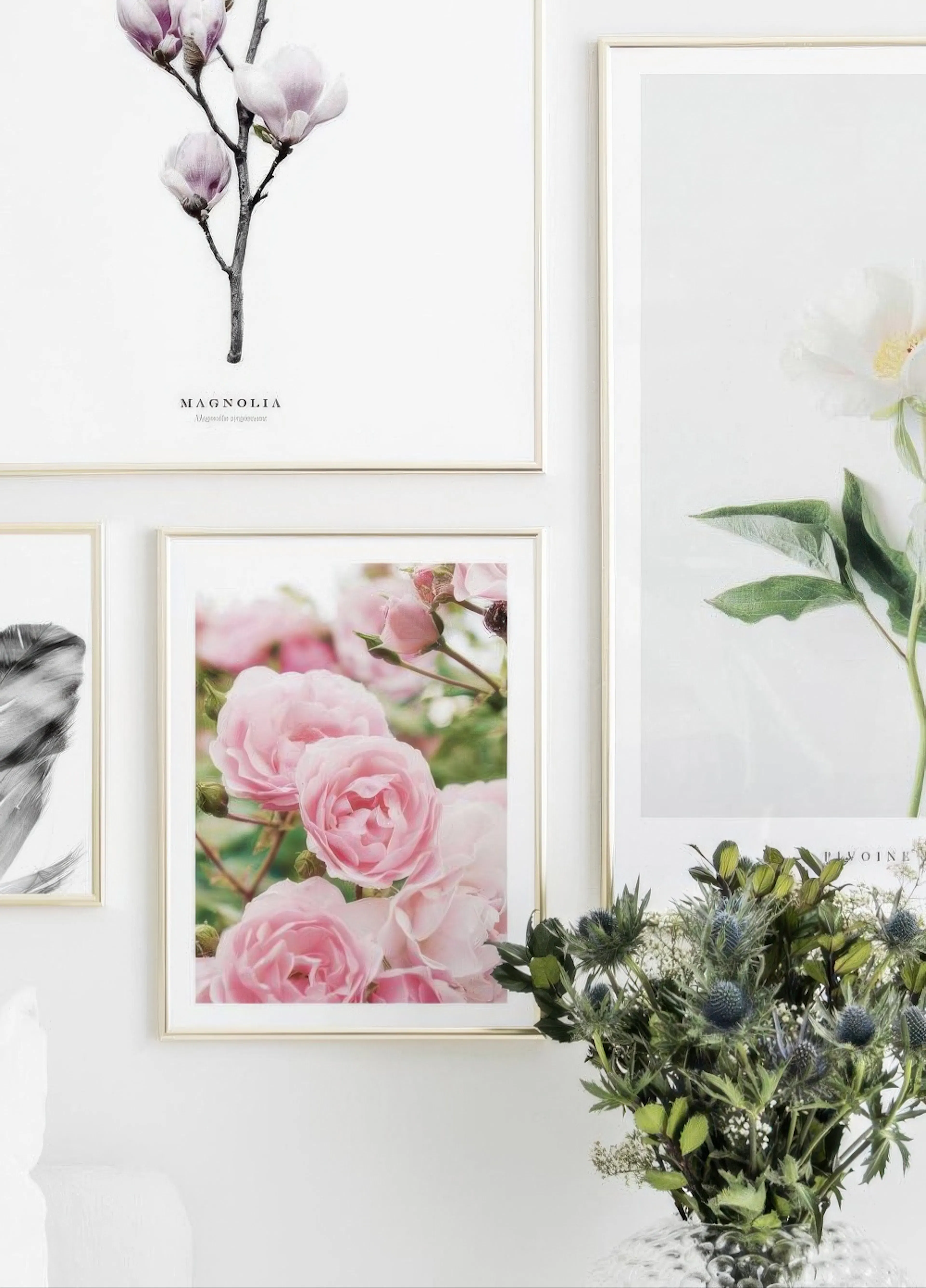 A gallery wall featuring a magnolia branch, white peony, and pink roses, with a vase of thistle and greenery nearby.