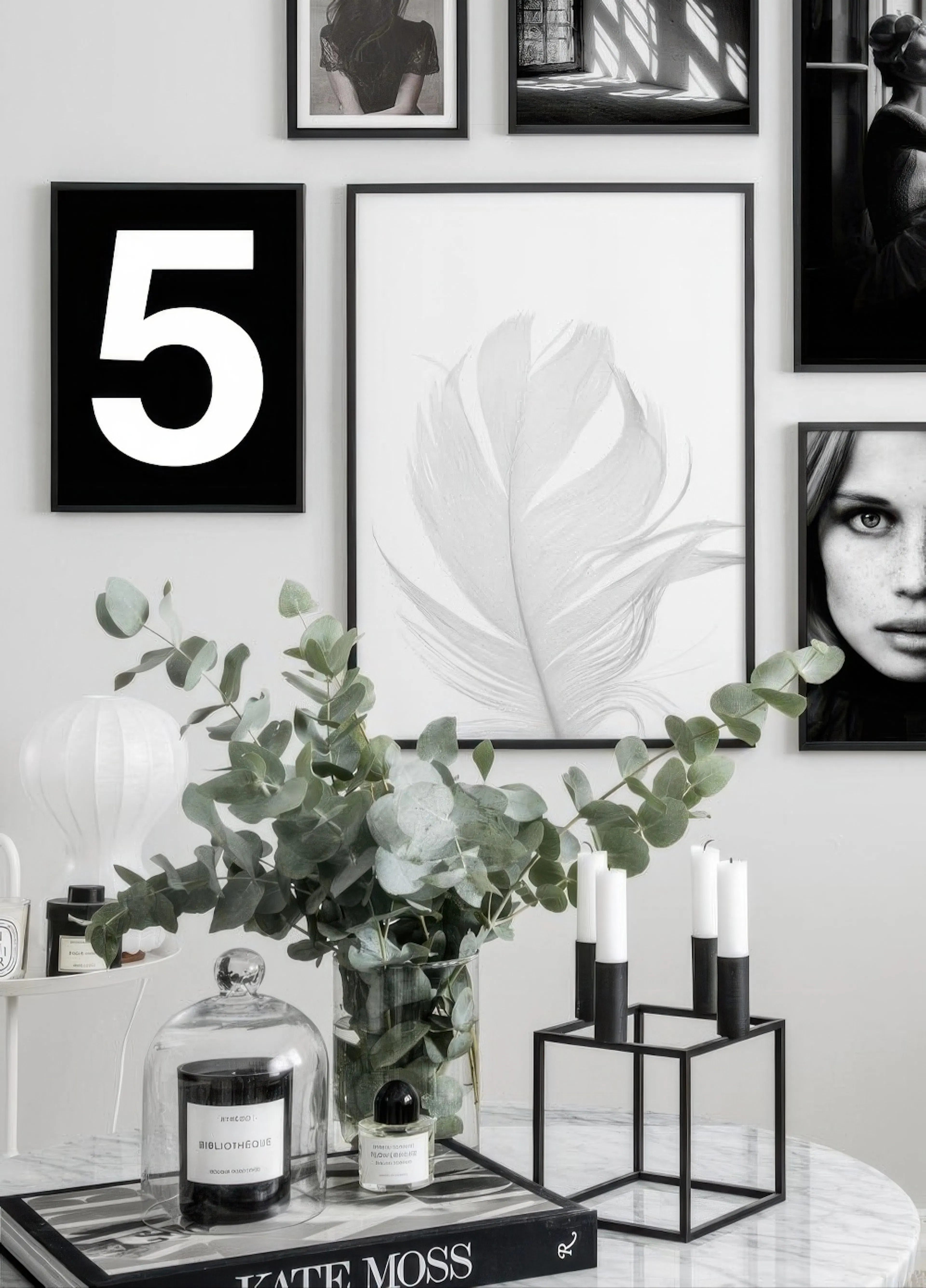 Valokuvajuliste vaaleasta höyhenestä, osana mustavalkoista tauluseinää modernissa olohuoneessa.