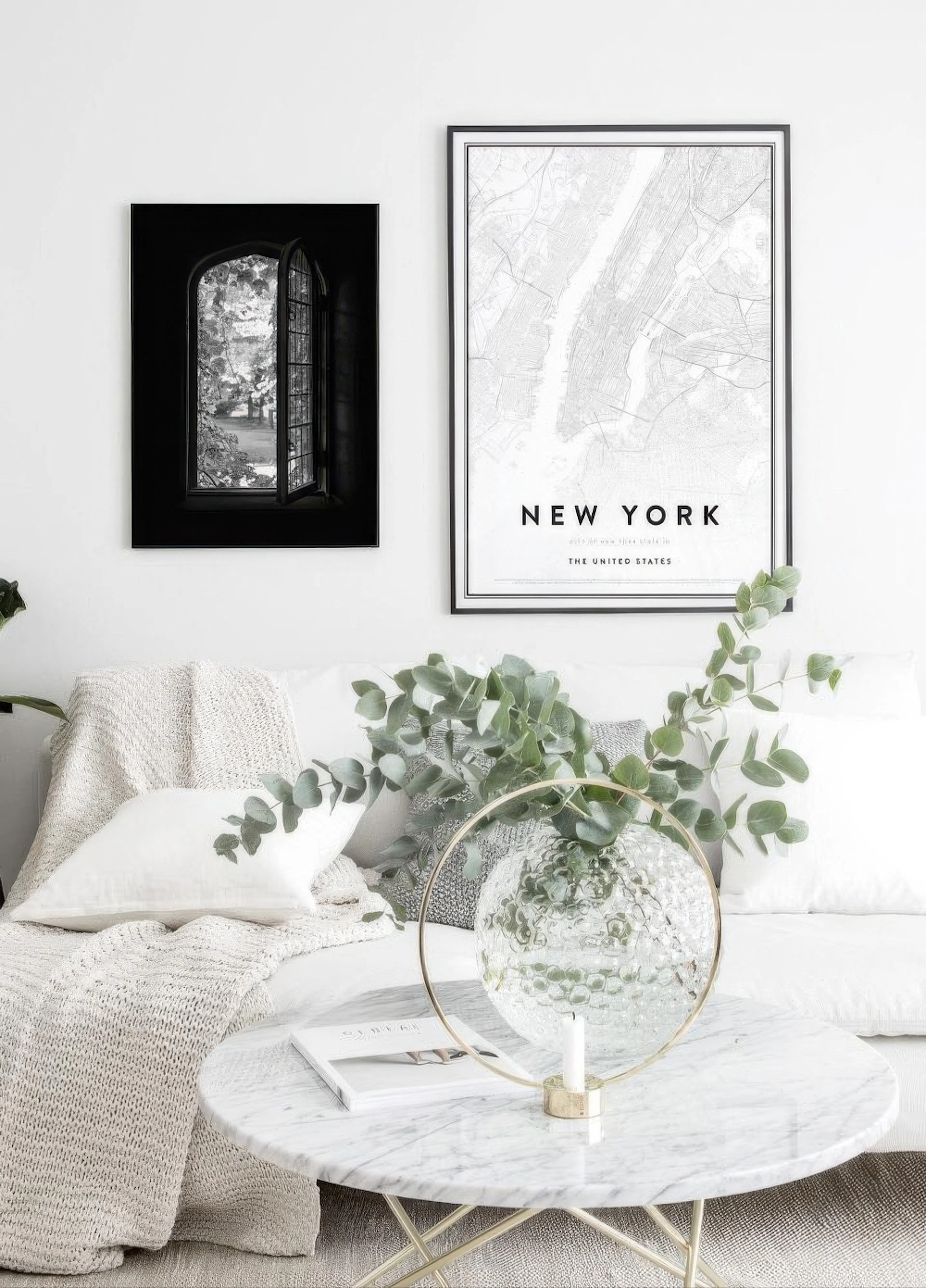 Mustavalkoinen juliste avonaisesta ikkunasta roikkuu valkoisella seinällä New York -karttajulisteen vieressä olohuoneessa sohvan