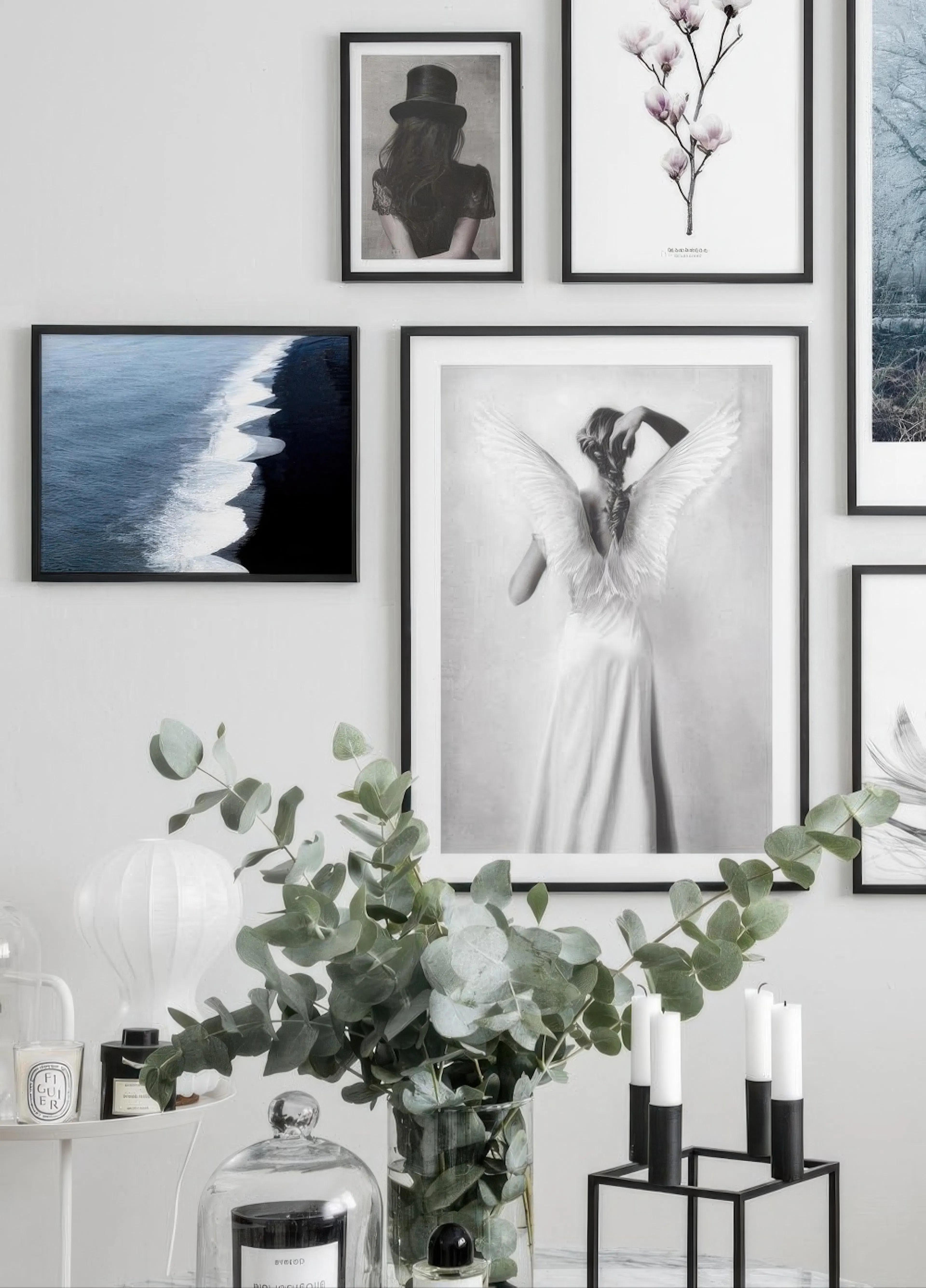 Nástěnná galerie plakátů s černobílou fotografií ženy s andělskými křídly, obrazy moře a květin, v elegantním obývacím pokoji.