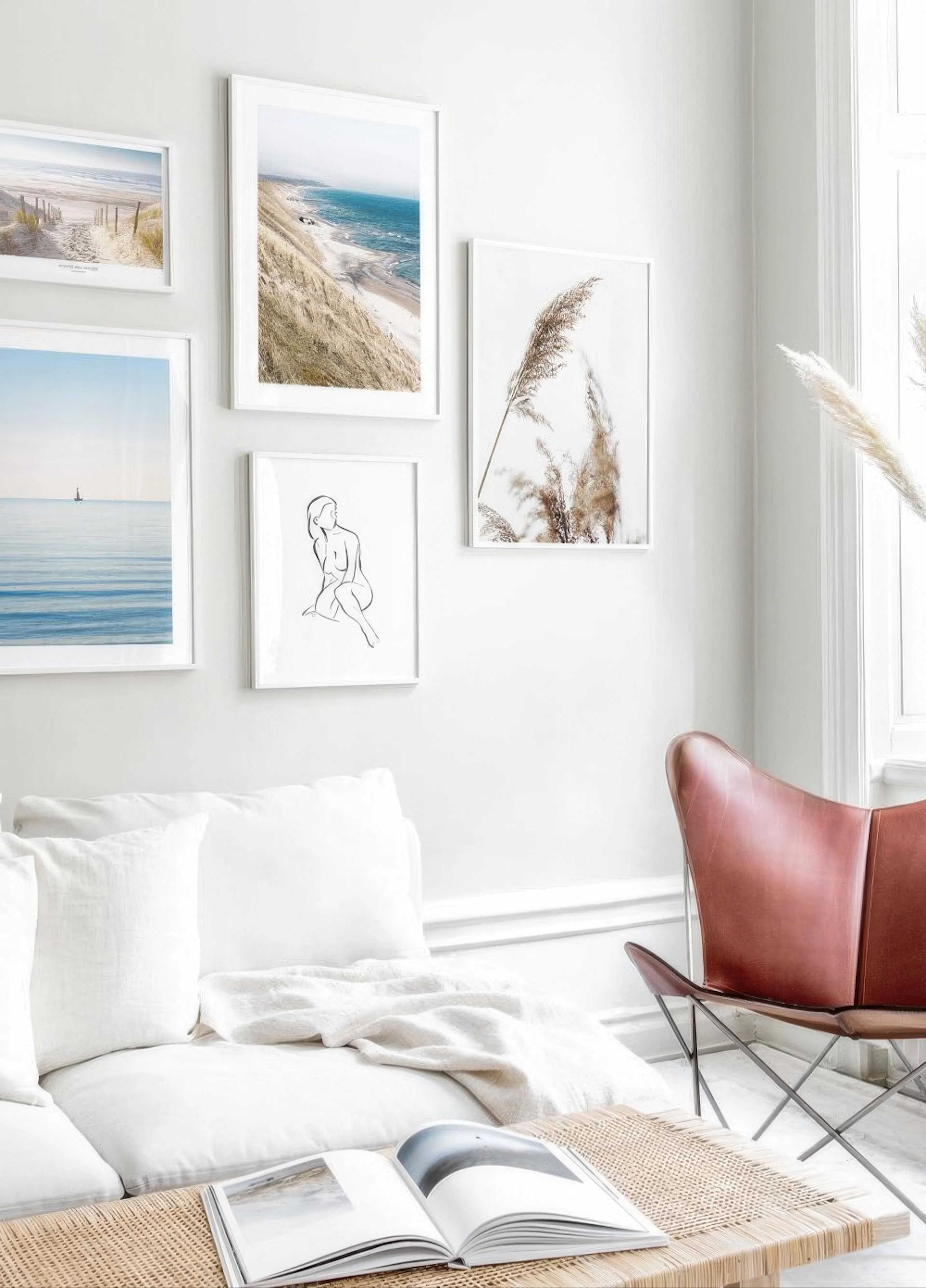 Viisi julistetta tauluseinällä olohuoneessa valkoisen sohvan yläpuolella. Kaksi julistetta esittää hiekkarantoja, yksi merta ja 