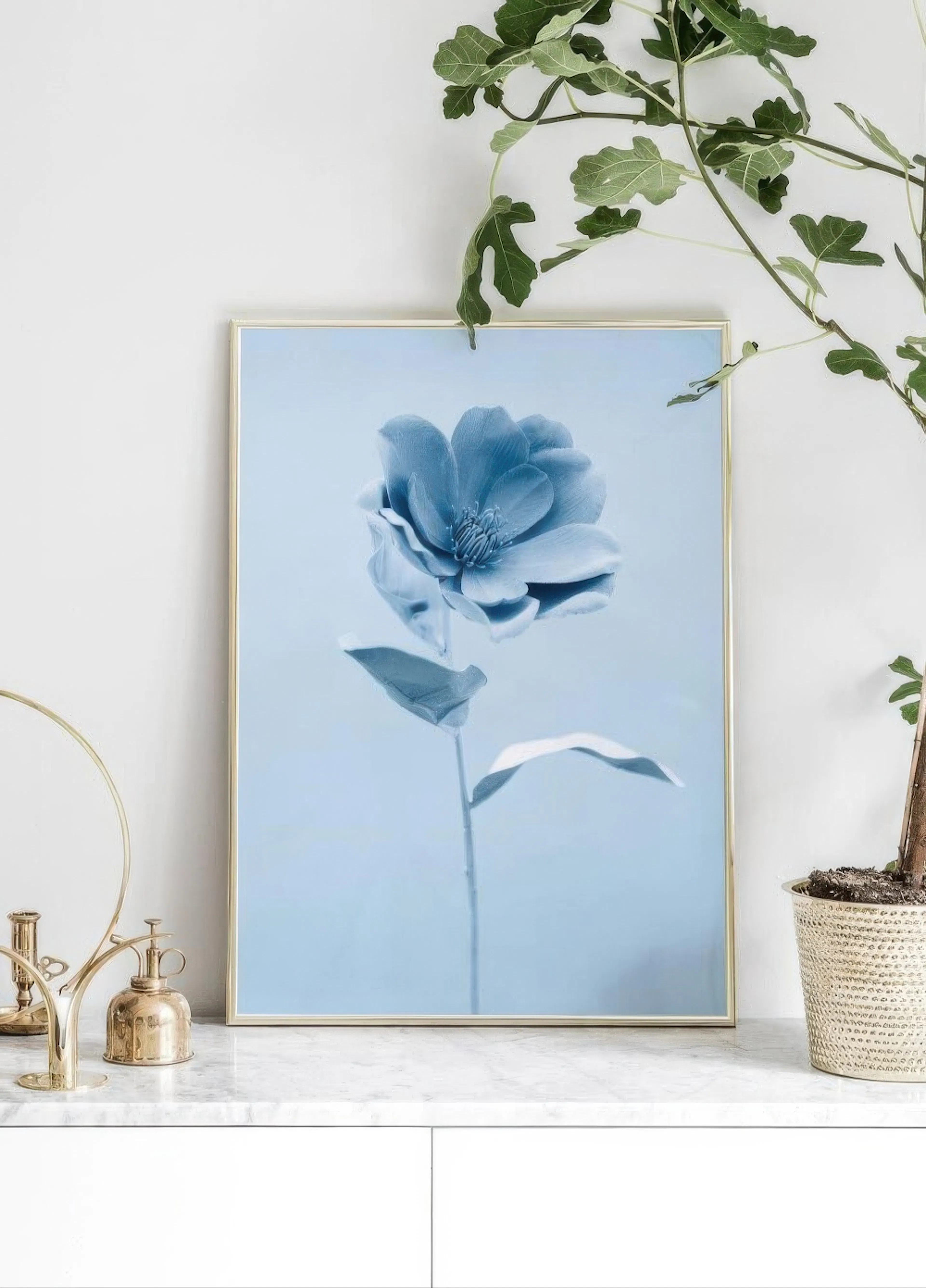 A poster of a single blue flower on a light blue background, displayed on a marble bench with a houseplant.