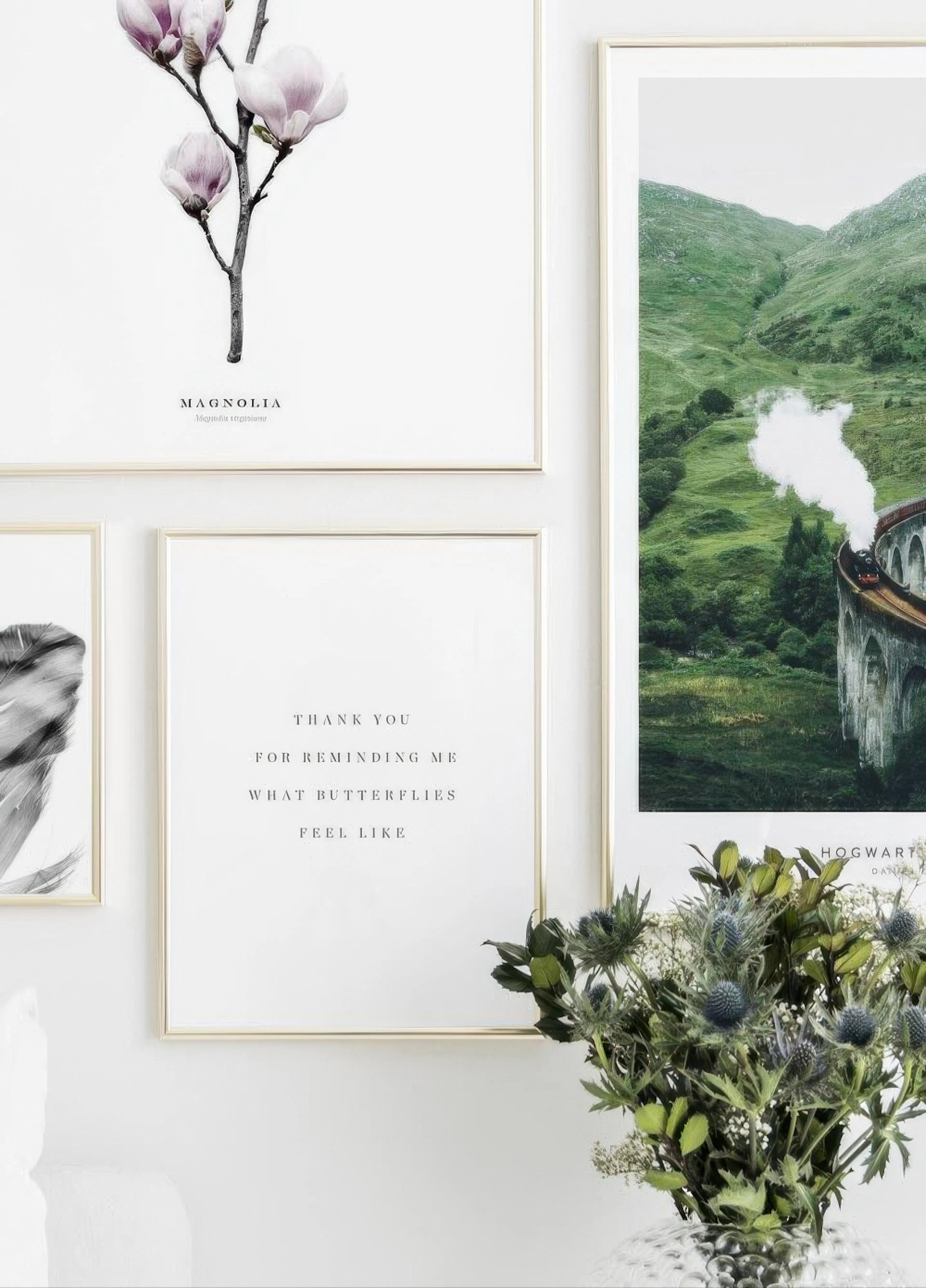 Nástěnná galerie plakátů: magnolie, citát, vlak na viaduktu a pírko, vedle kytice modrých bodláků.