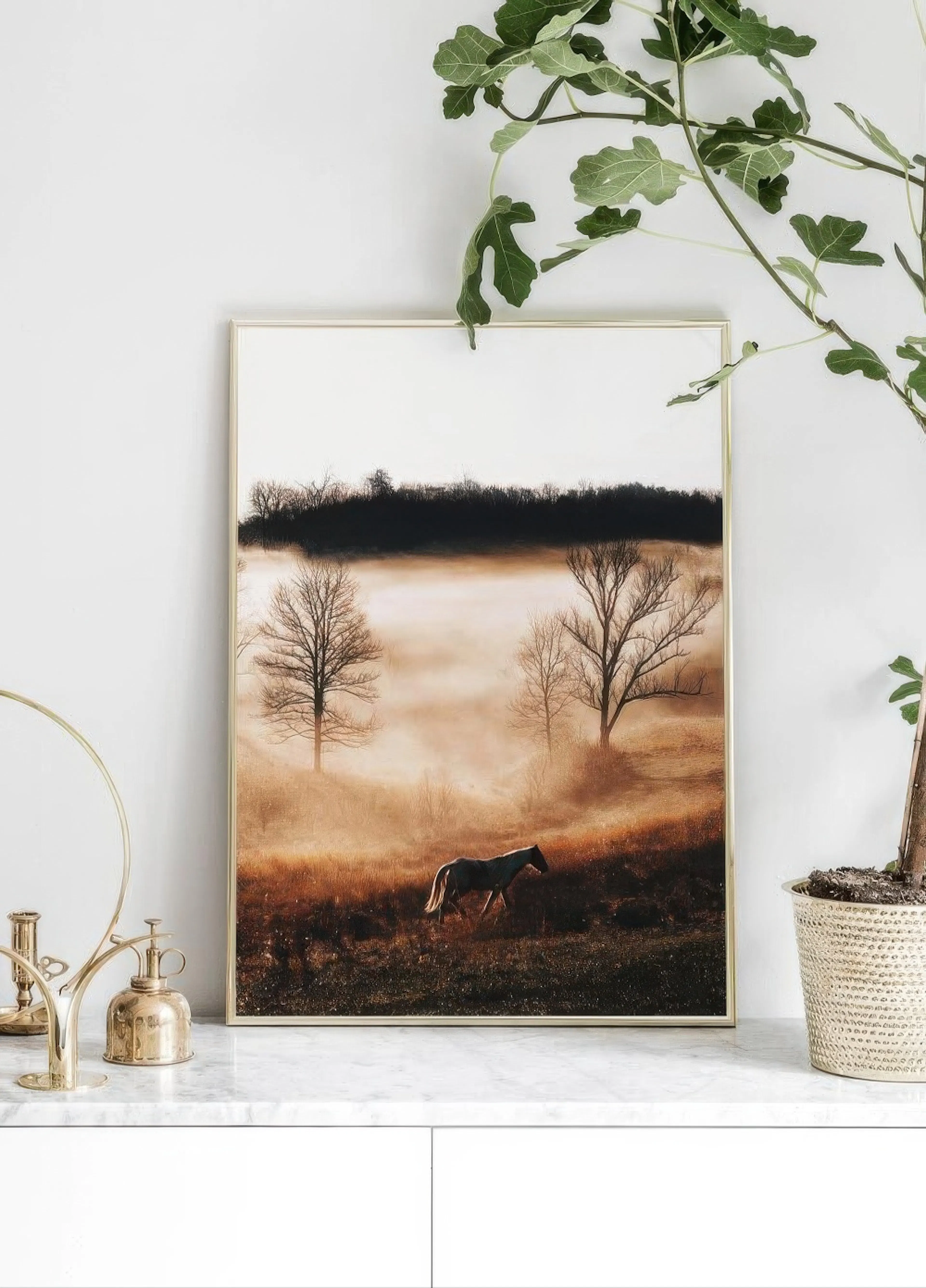 A poster of a horse in a misty field at sunrise, with bare trees, displayed on a marble surface with a plant.