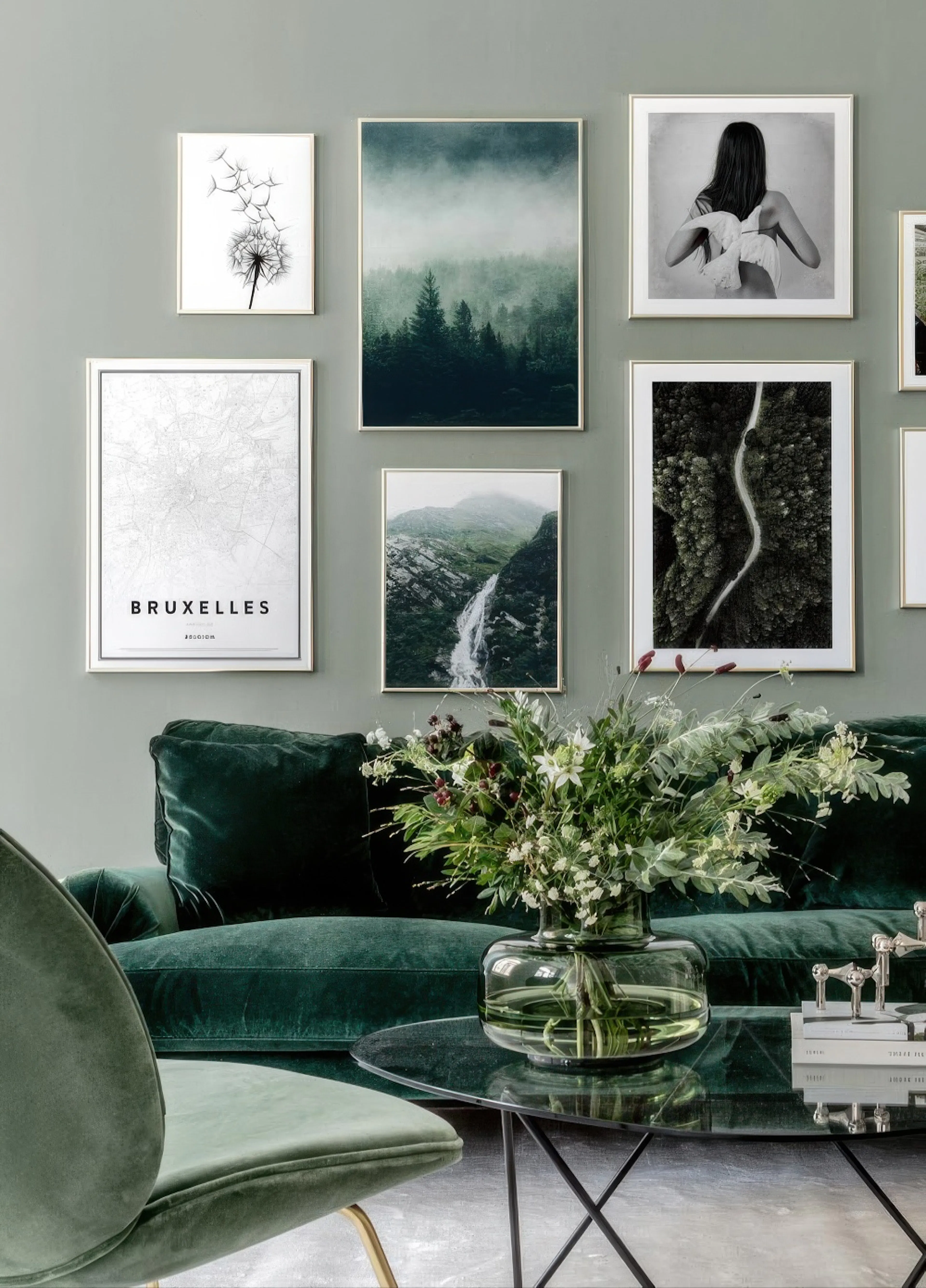 Eine Bilderwand mit Postern von Naturmotiven, einer Stadtkarte von Brüssel und einer Frau, über einem grünen Sofa.