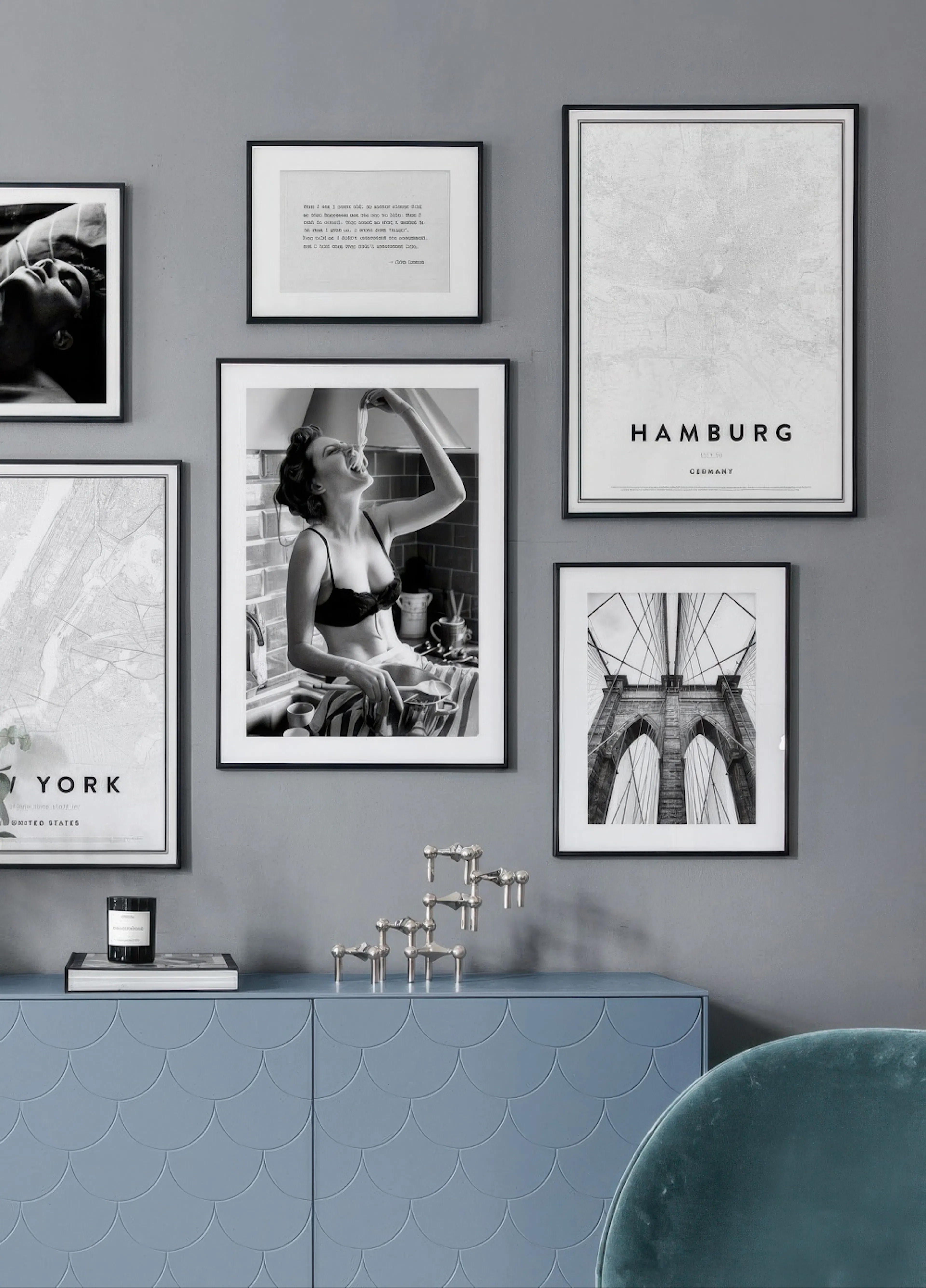 A gallery wall with various posters, including a woman eating spaghetti, city maps of New York and Hamburg, and the Brooklyn Bri