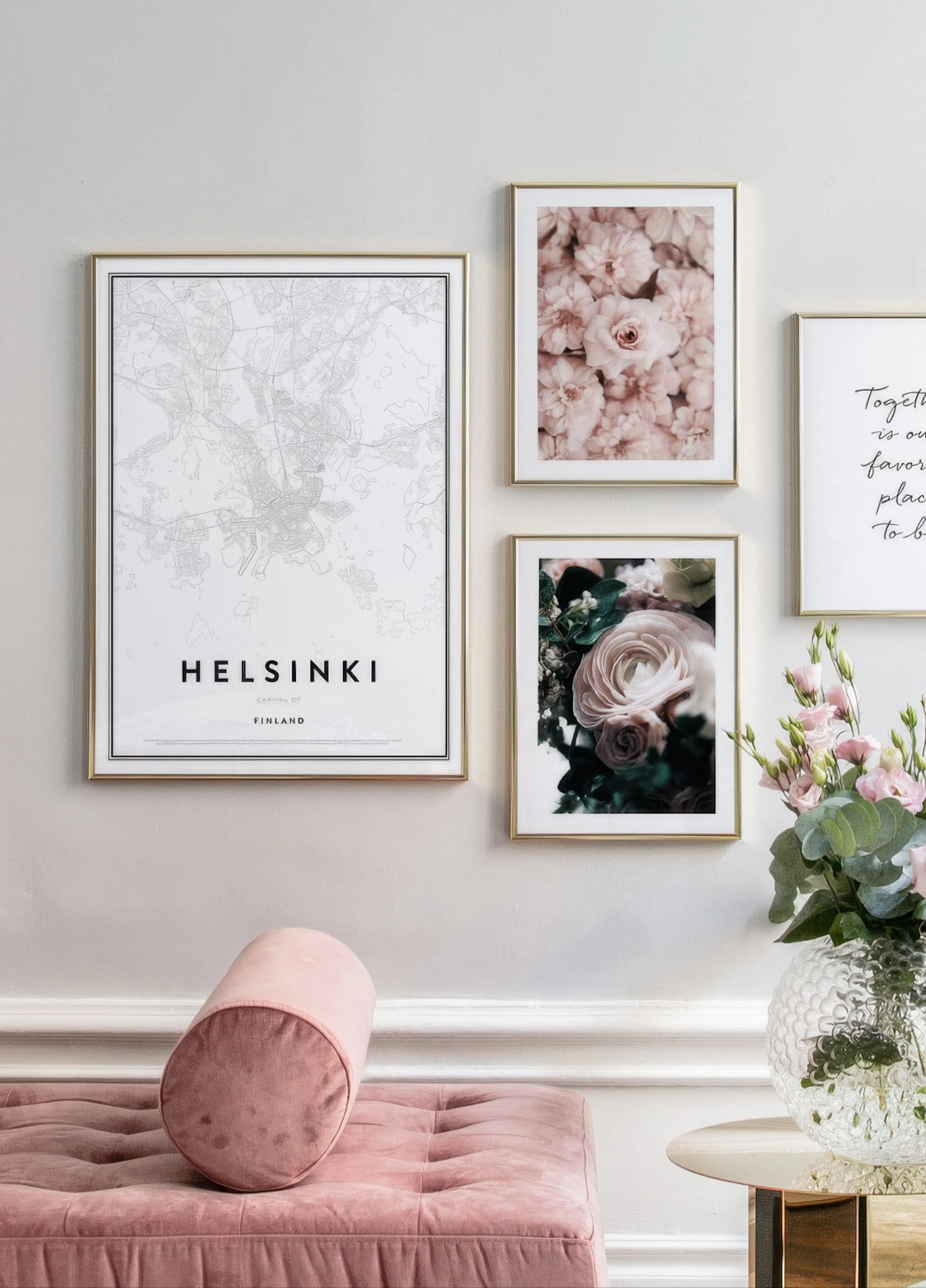 A gallery wall of posters above a pink velvet bench, featuring a Helsinki map, pink flowers, and a quote.