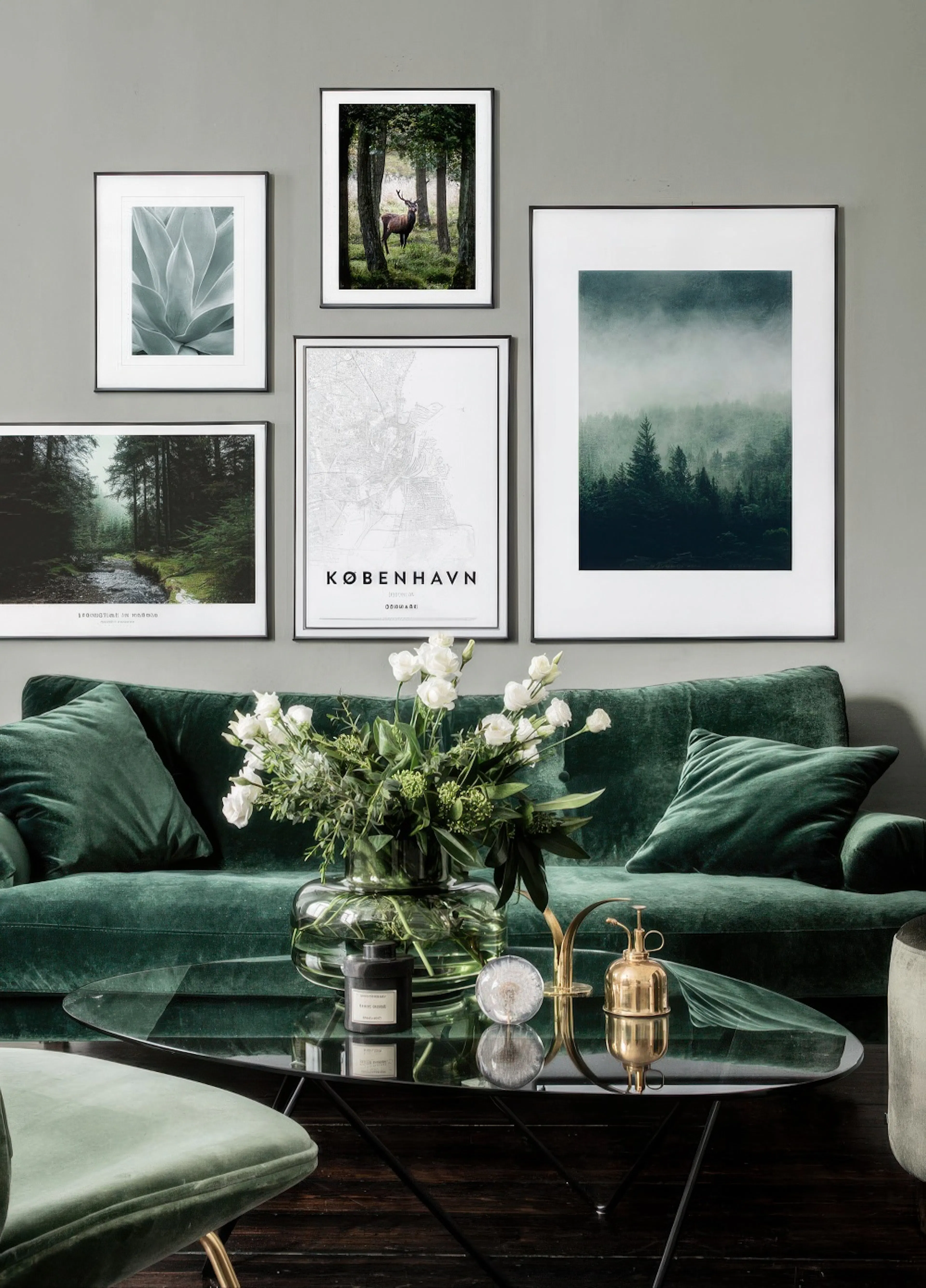 A gallery wall with five posters above a green velvet sofa. Posters include a stag, forest, misty pines, succulent, and a Copenh