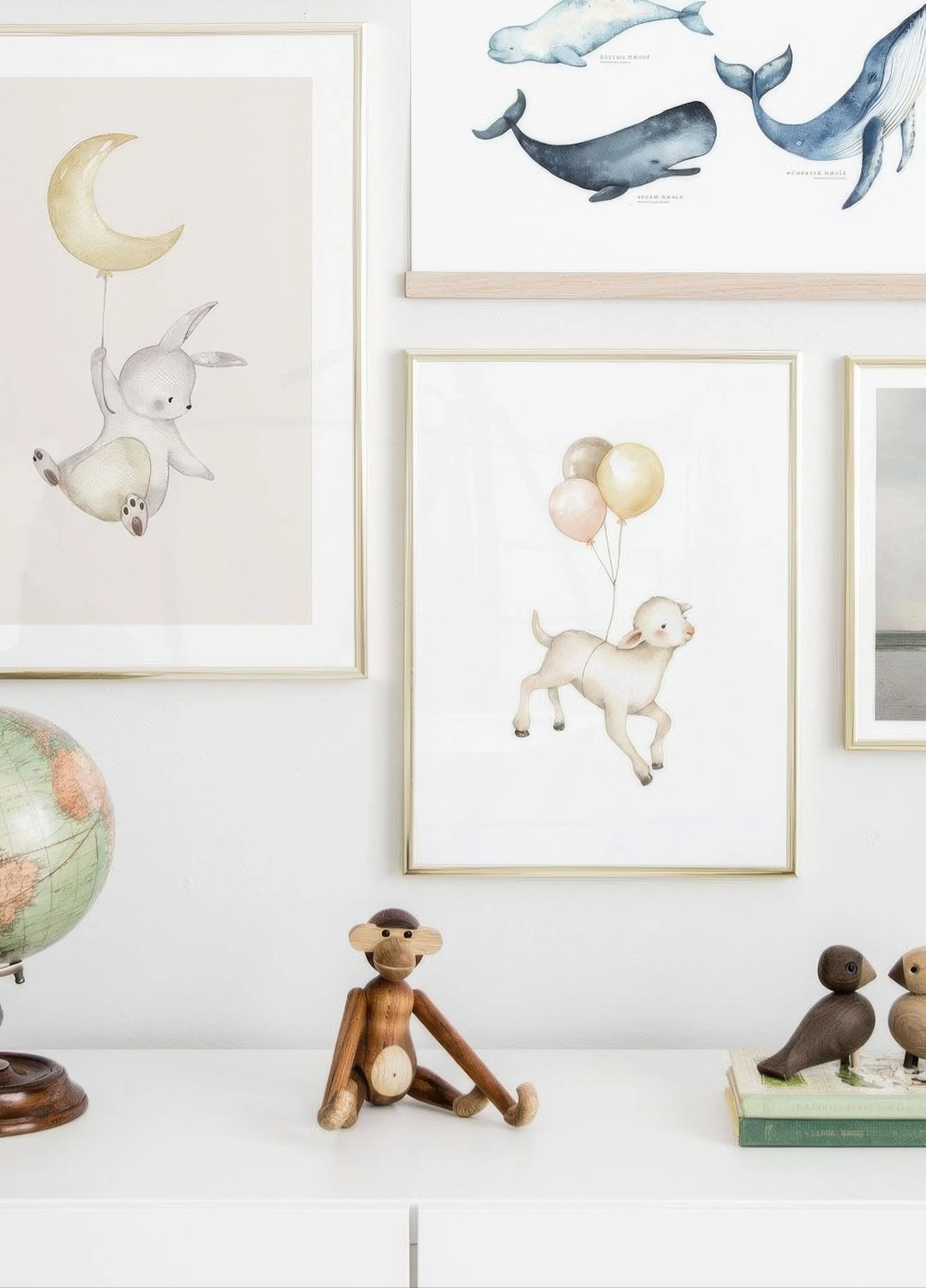 A gallery wall featuring a watercolour print of a bunny holding a moon, a lamb with balloons, and a whale chart, displayed above