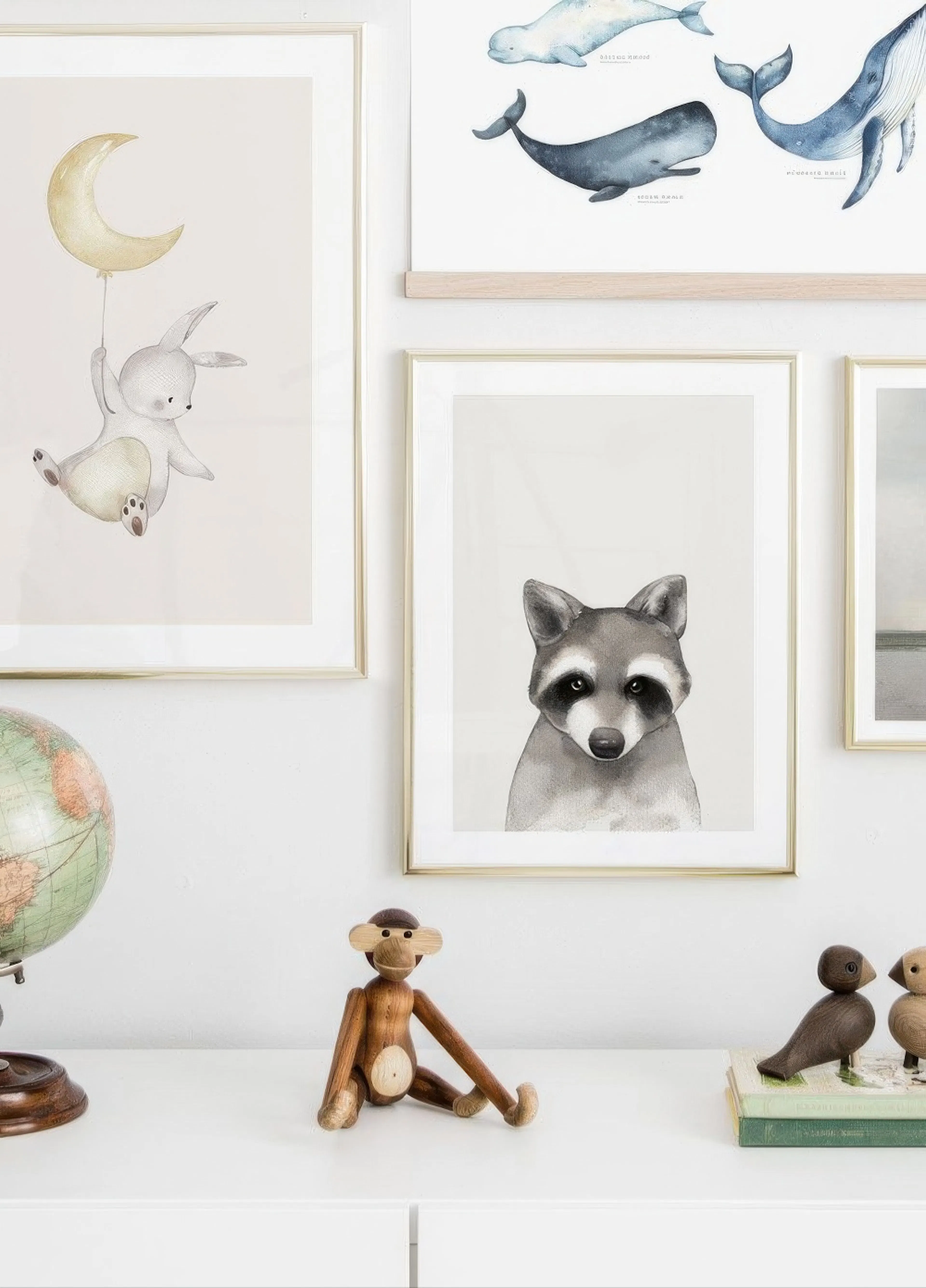 A gallery wall featuring a rabbit holding a moon balloon, a realistic raccoon, and a whale chart in a childs room.