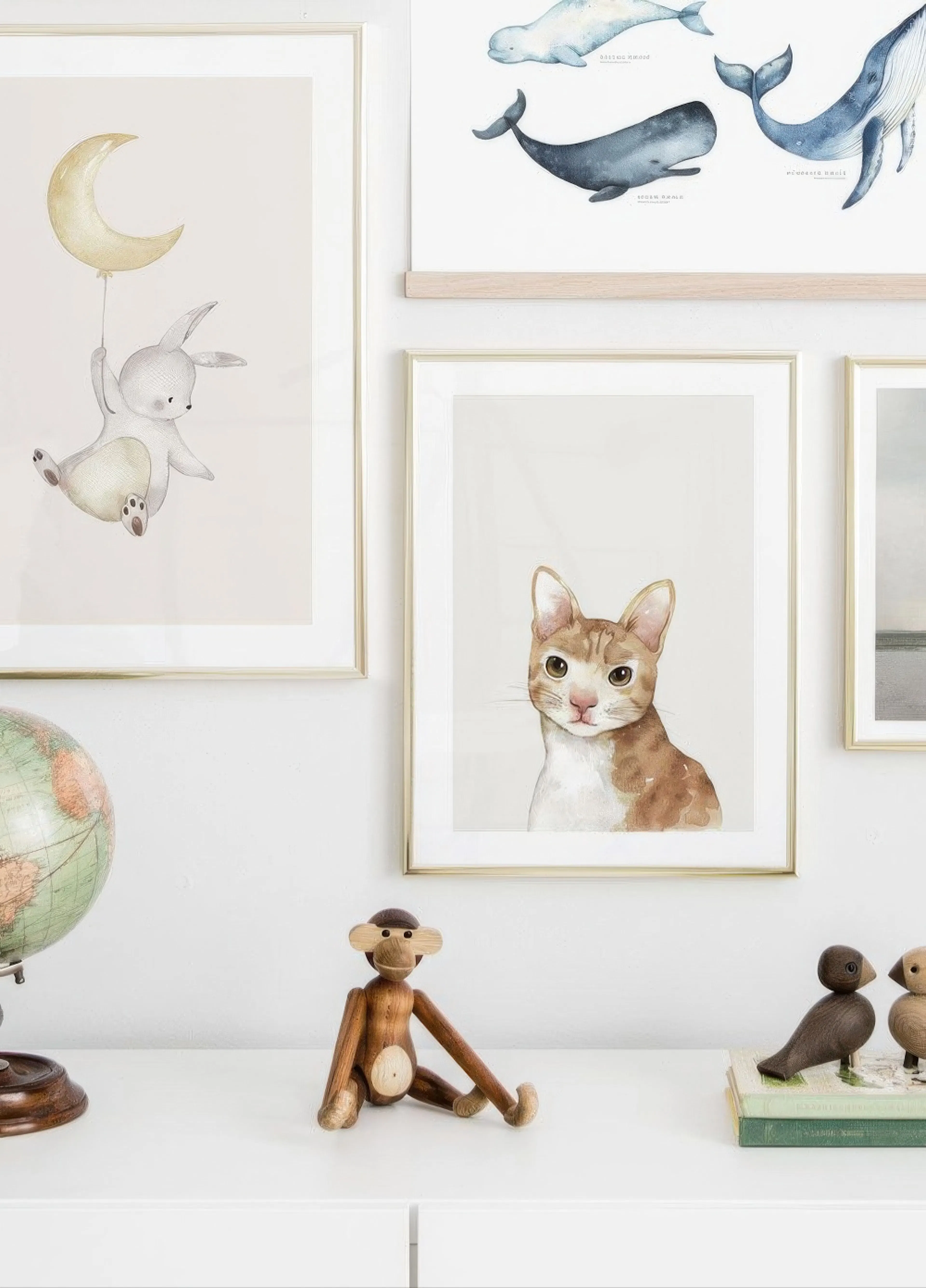 A gallery wall featuring a watercolour print of a flying bunny with a crescent moon balloon, and a cat, above a white cabinet wi