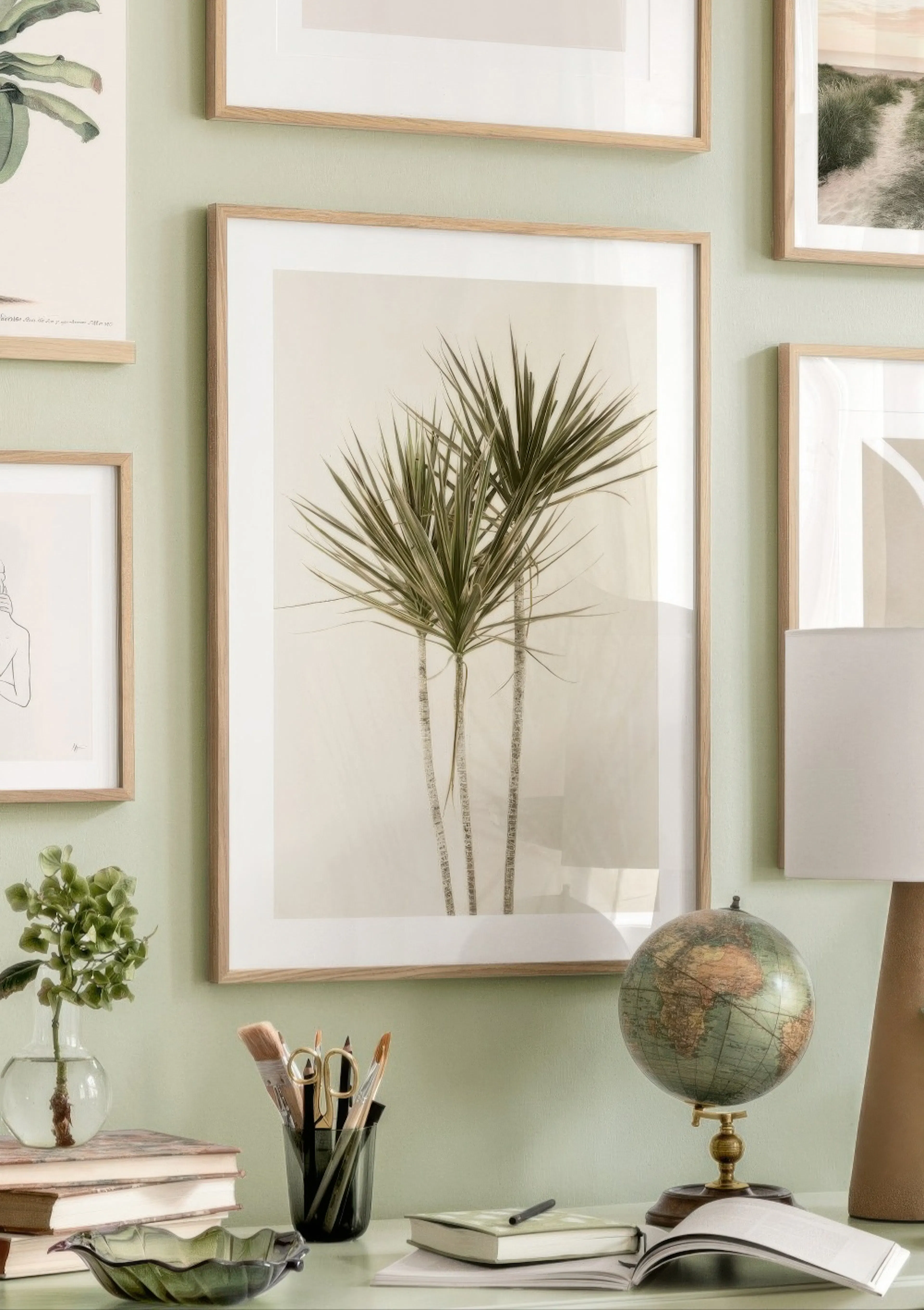 A botanical poster of three palm-like plants with spiky leaves on a light background, displayed in a gallery wall setting above 