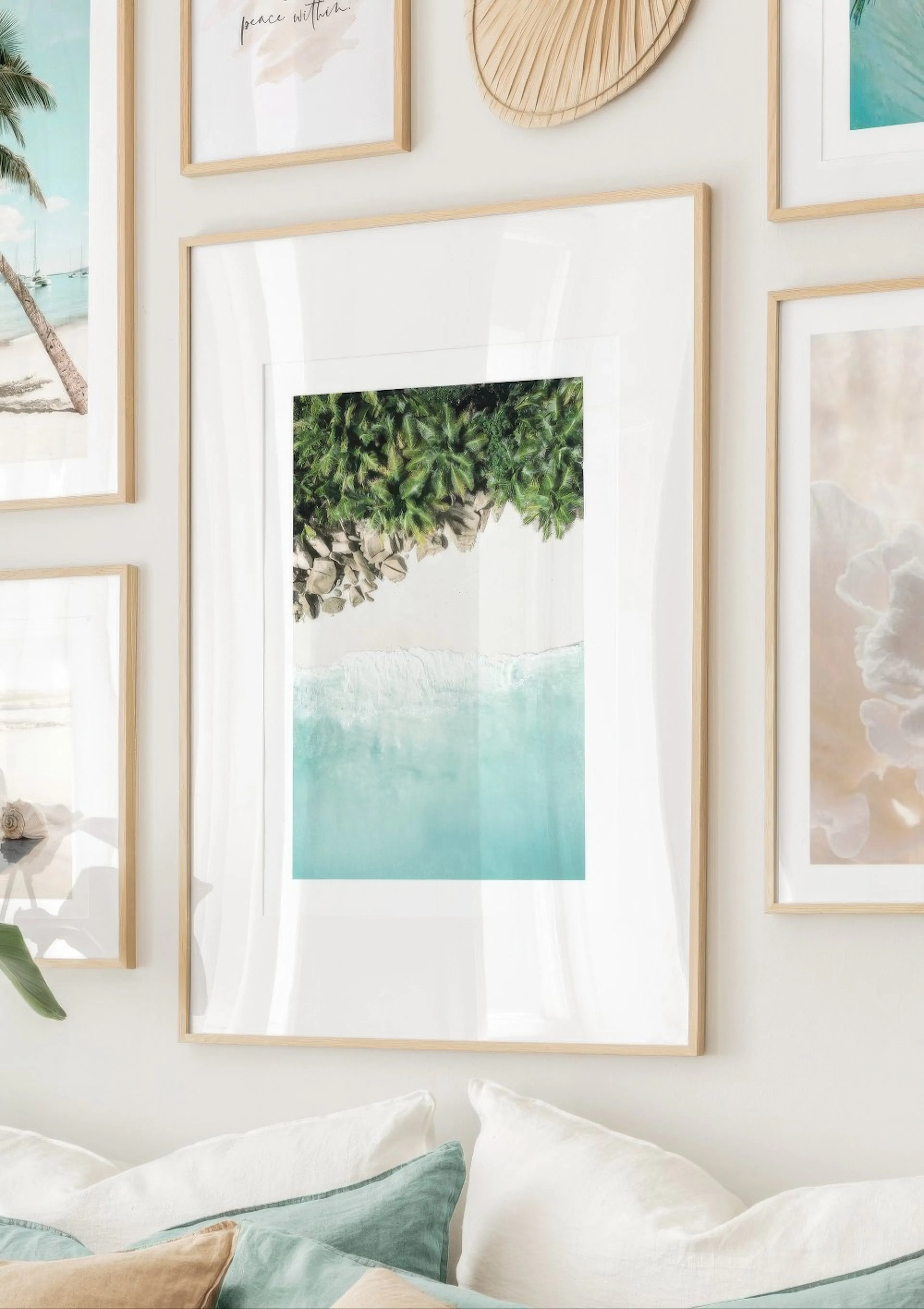 An aerial tropical poster with a white sand beach, lush green palms, and turquoise ocean waves, displayed above a sofa.