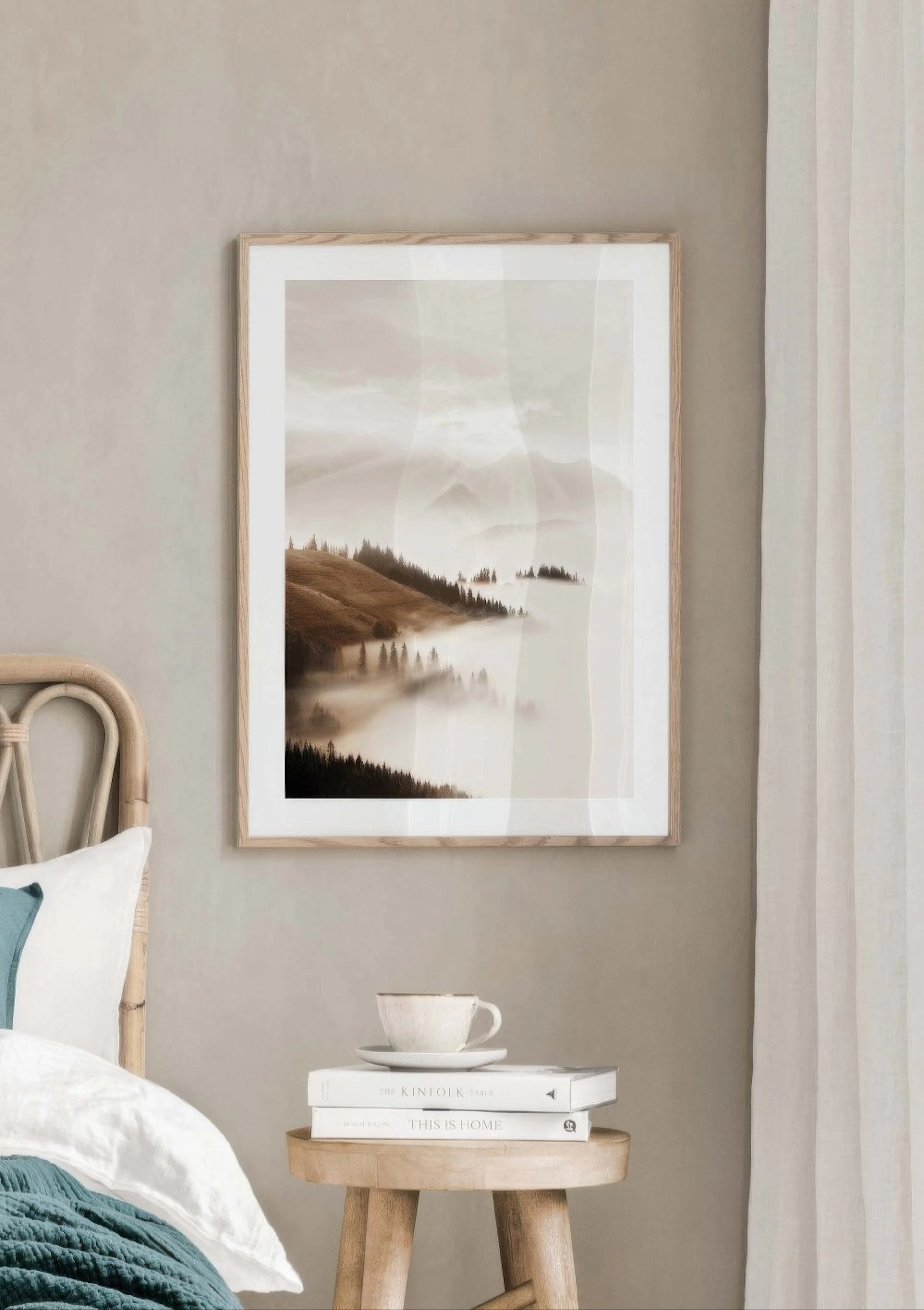A poster displaying a misty mountain landscape with fog-covered trees, hanging above a bedside table in a bedroom.