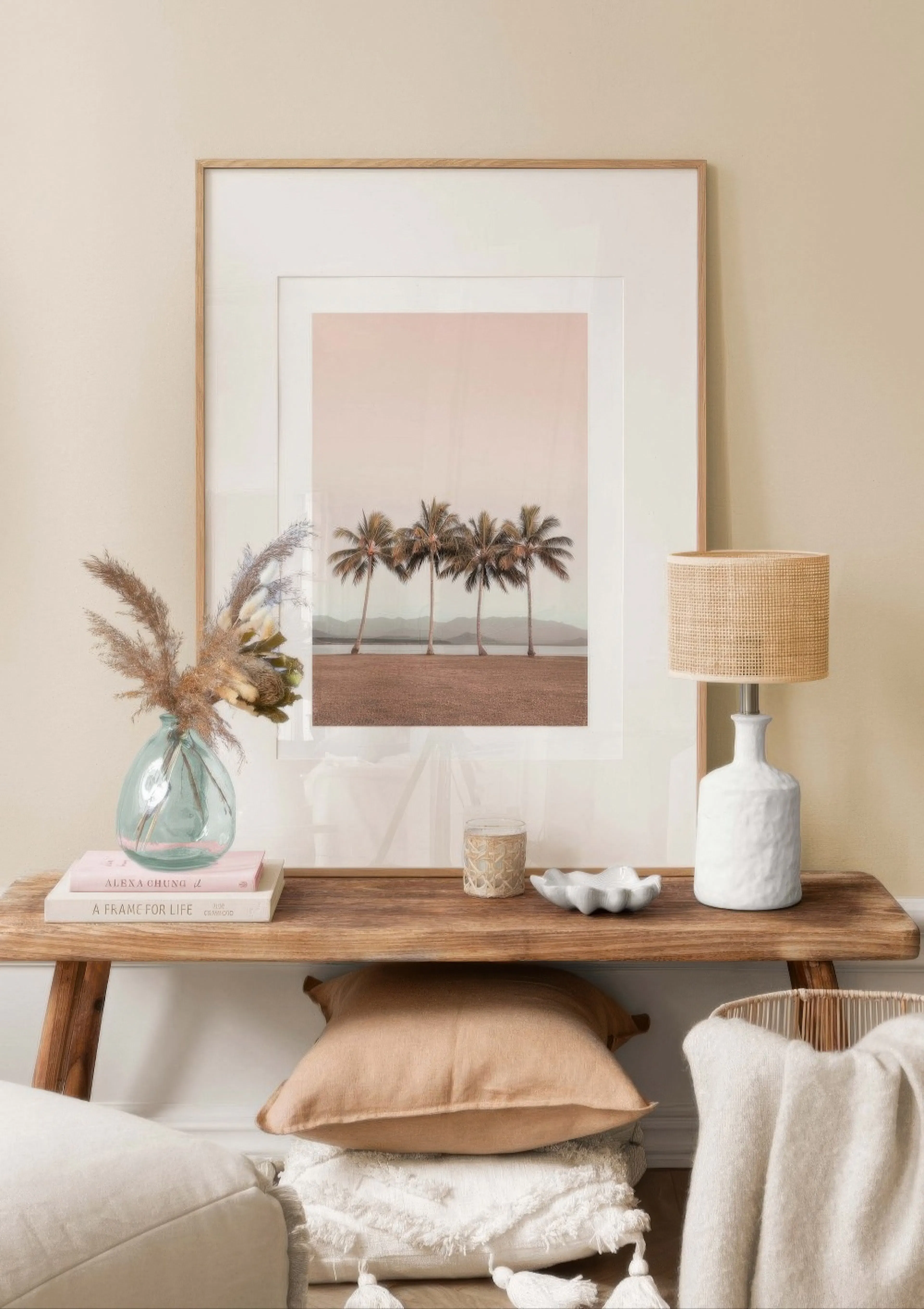 A poster of five palm trees on a beach with mountains and water in the background, displayed on a wooden console table with a la