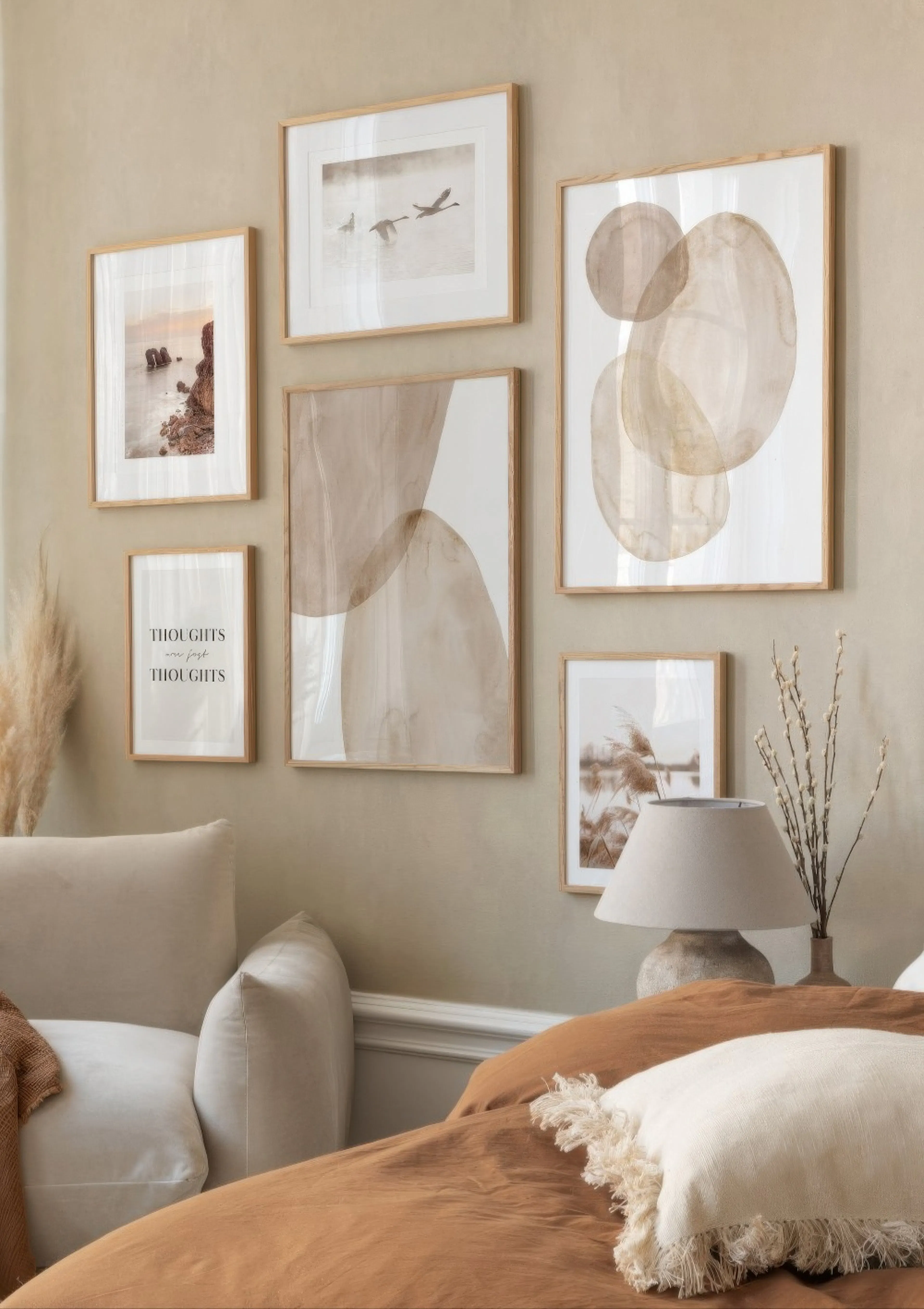 A gallery wall of neutral-toned posters, including abstract shapes, a seascape, flying swans, reeds, and text, displayed above a