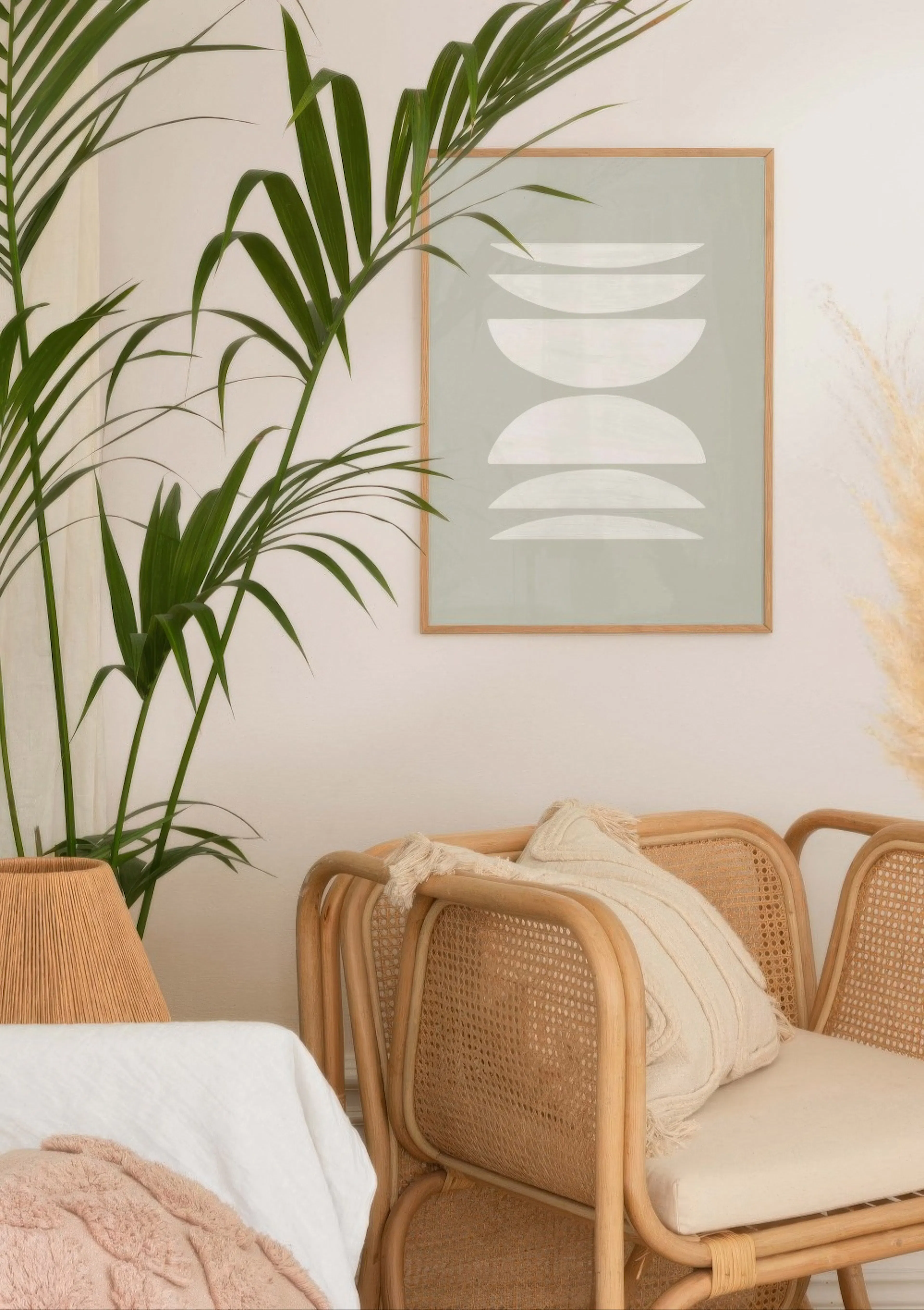 Pale green poster with white abstract crescent shapes, hanging above a natural rattan chair in a bright room.
