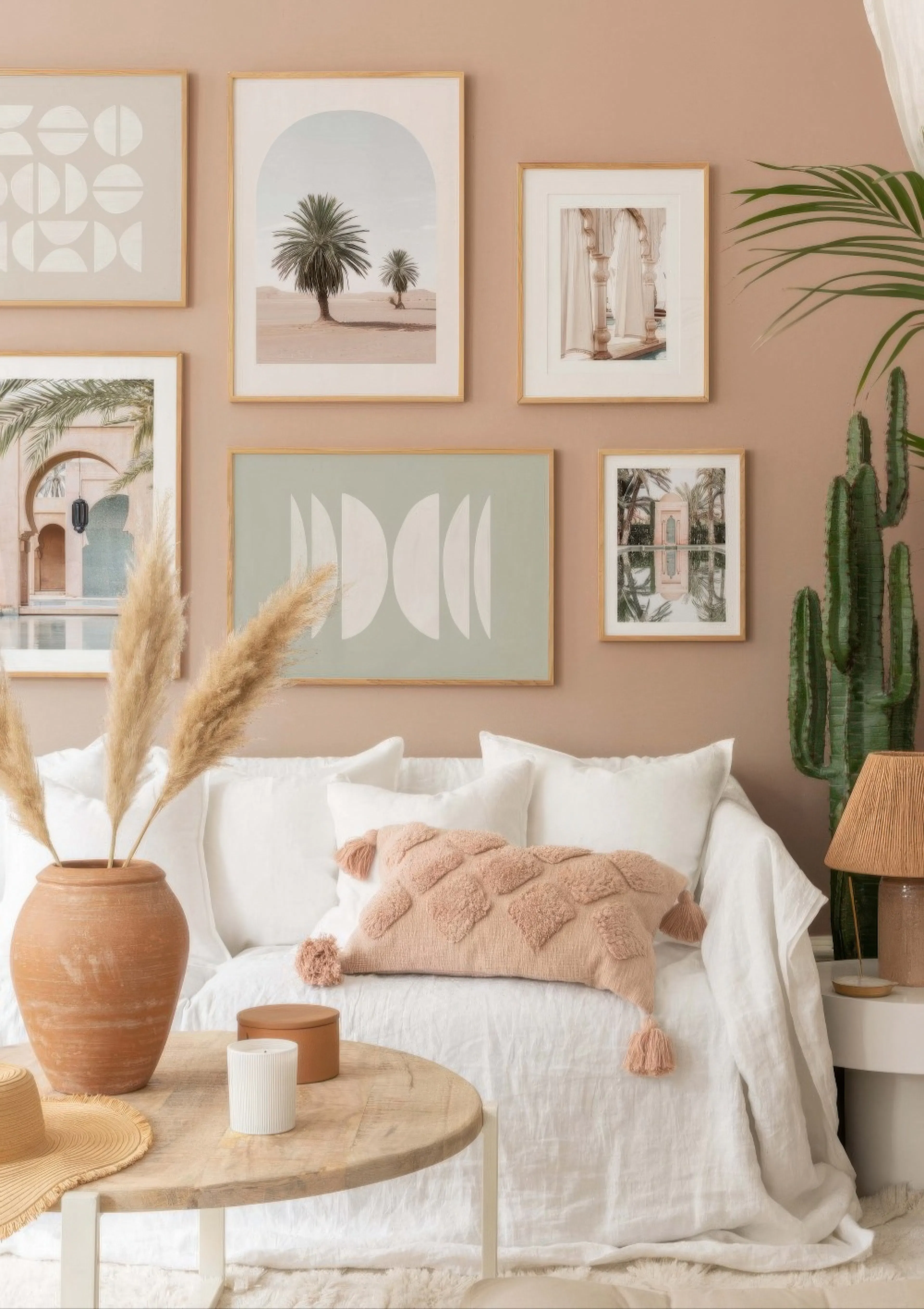 A gallery wall with five posters above a white sofa, featuring desert landscapes, architectural details, and geometric shapes.