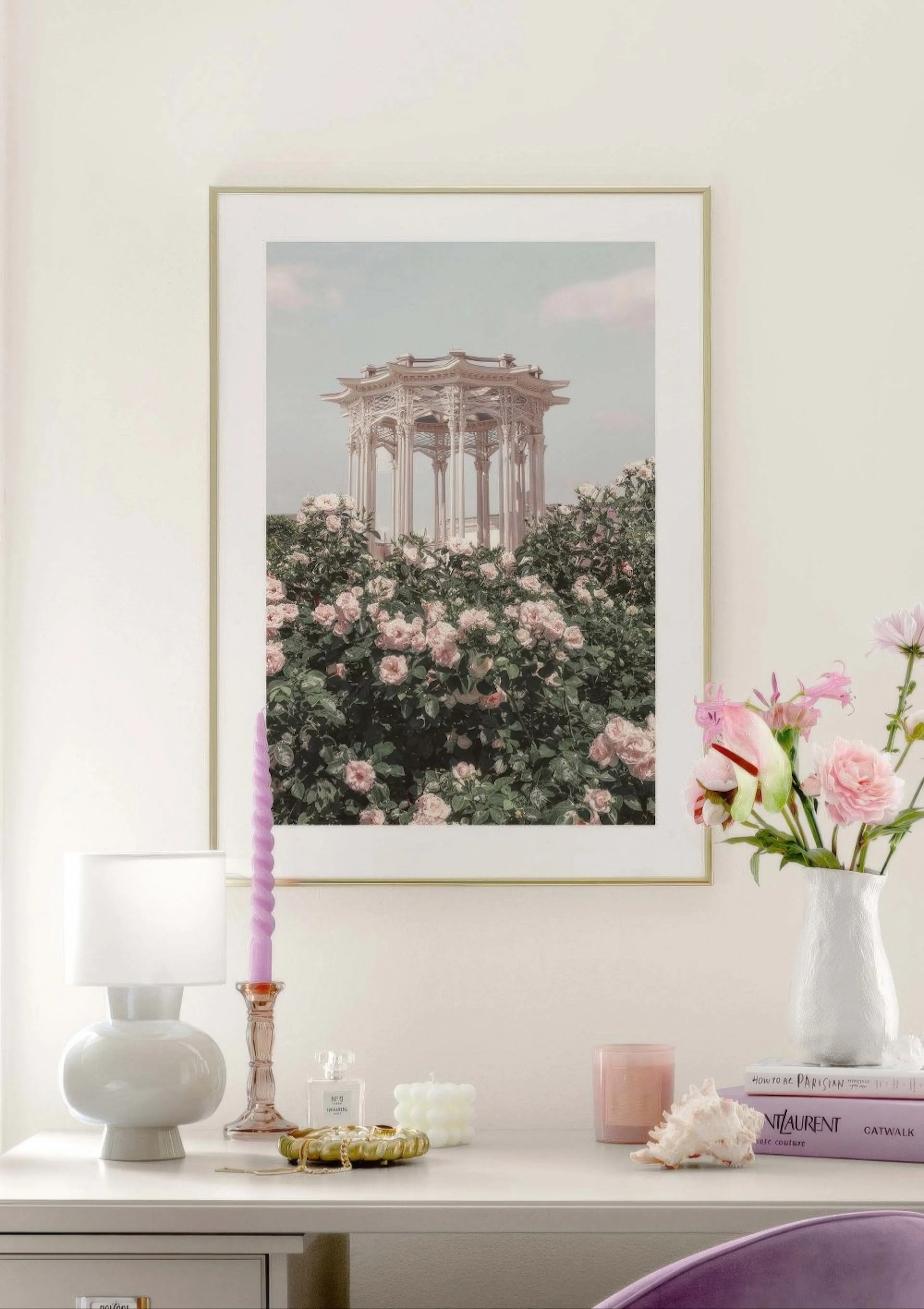 Poster con un gazebo bianco in stile asiatico tra cespugli di rose rosa, esposto sopra una scrivania con lampada, candele e fior