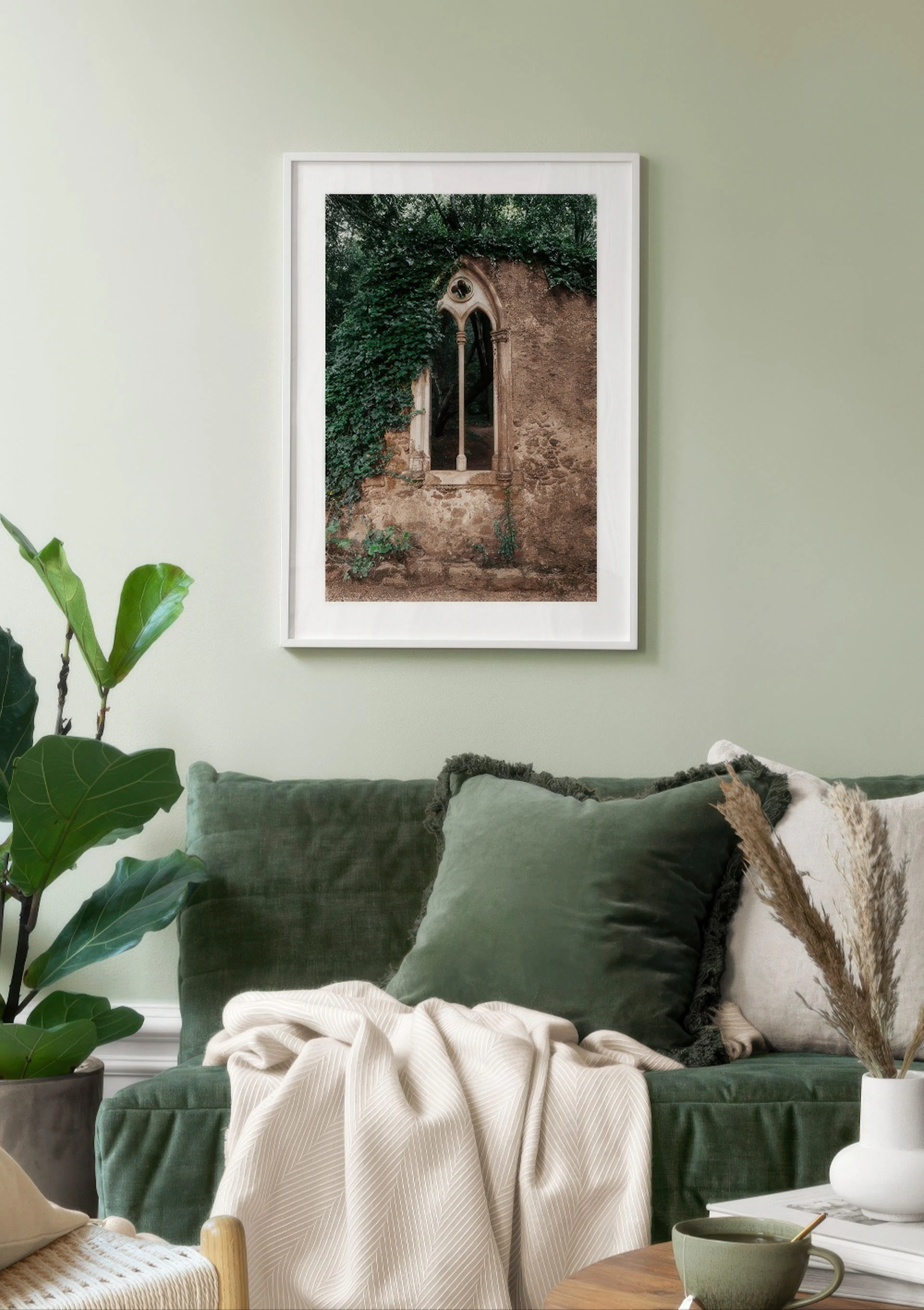Poster con finestra gotica in pietra antica ricoperta di edera, appeso sopra un divano verde con cuscini.