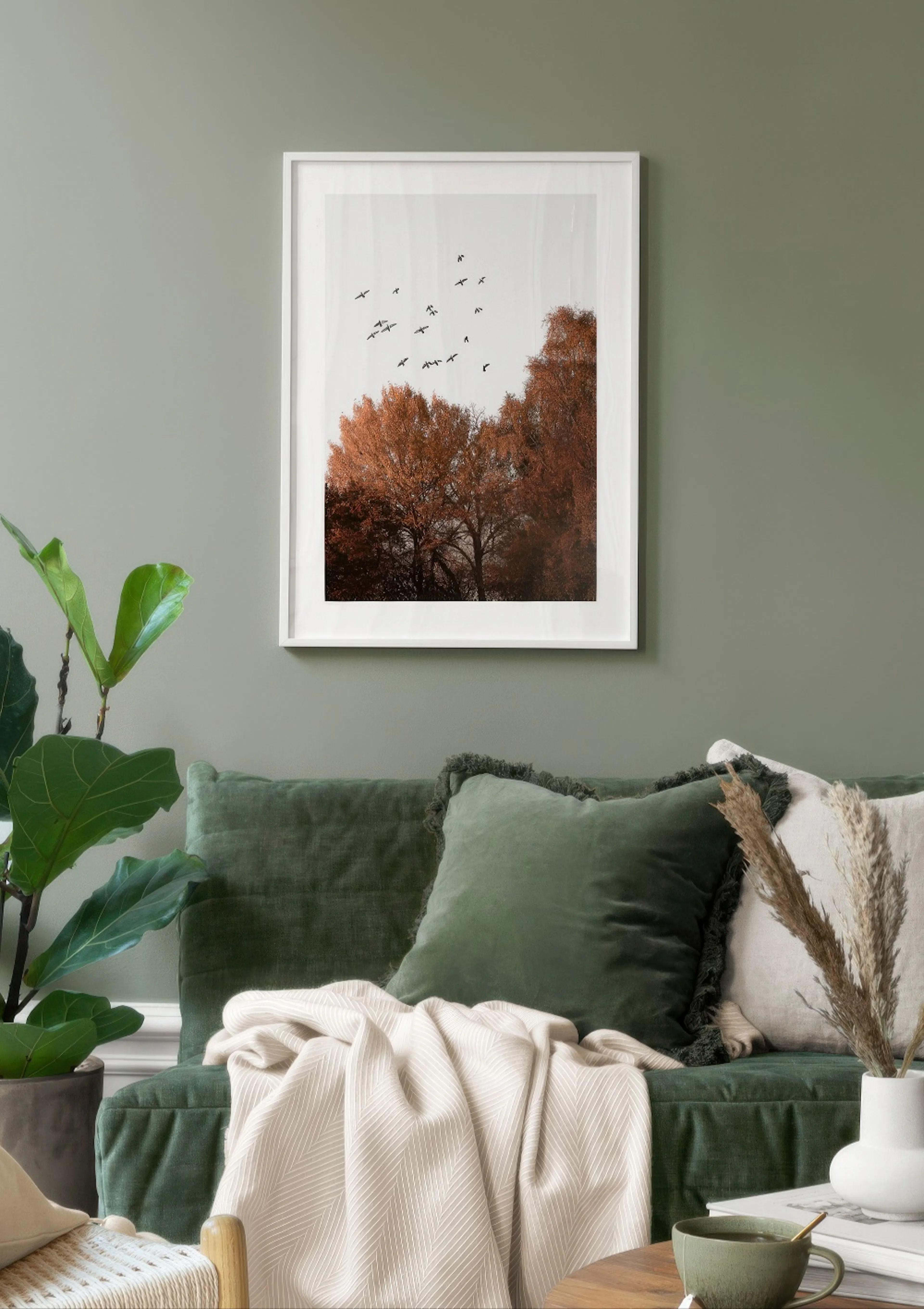 A poster featuring a flock of birds flying over autumn trees with orange leaves, displayed above a green sofa.