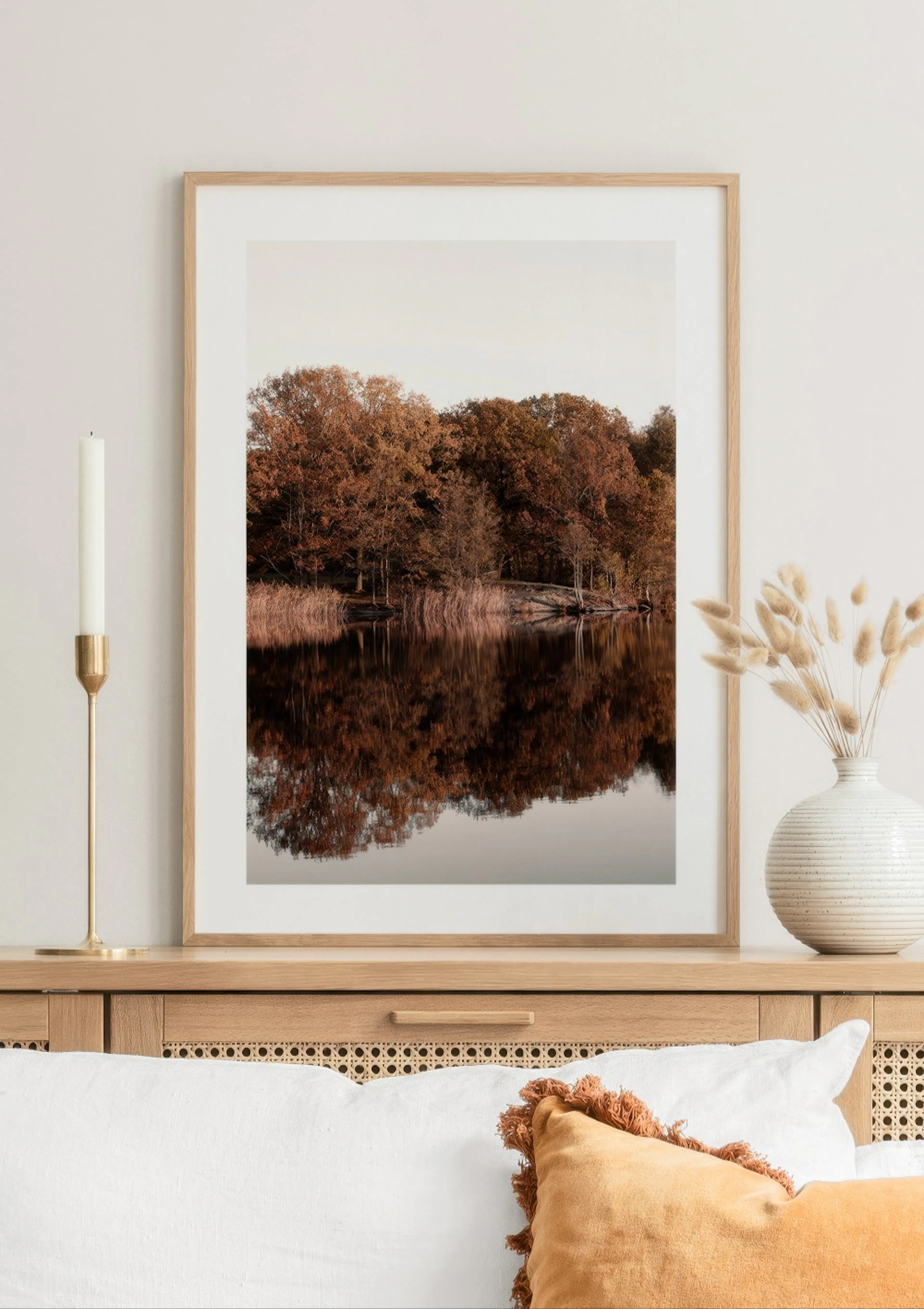 Poster mit Herbstwald-Spiegelung auf einem See, über einem Holzschrank mit Dekoration.