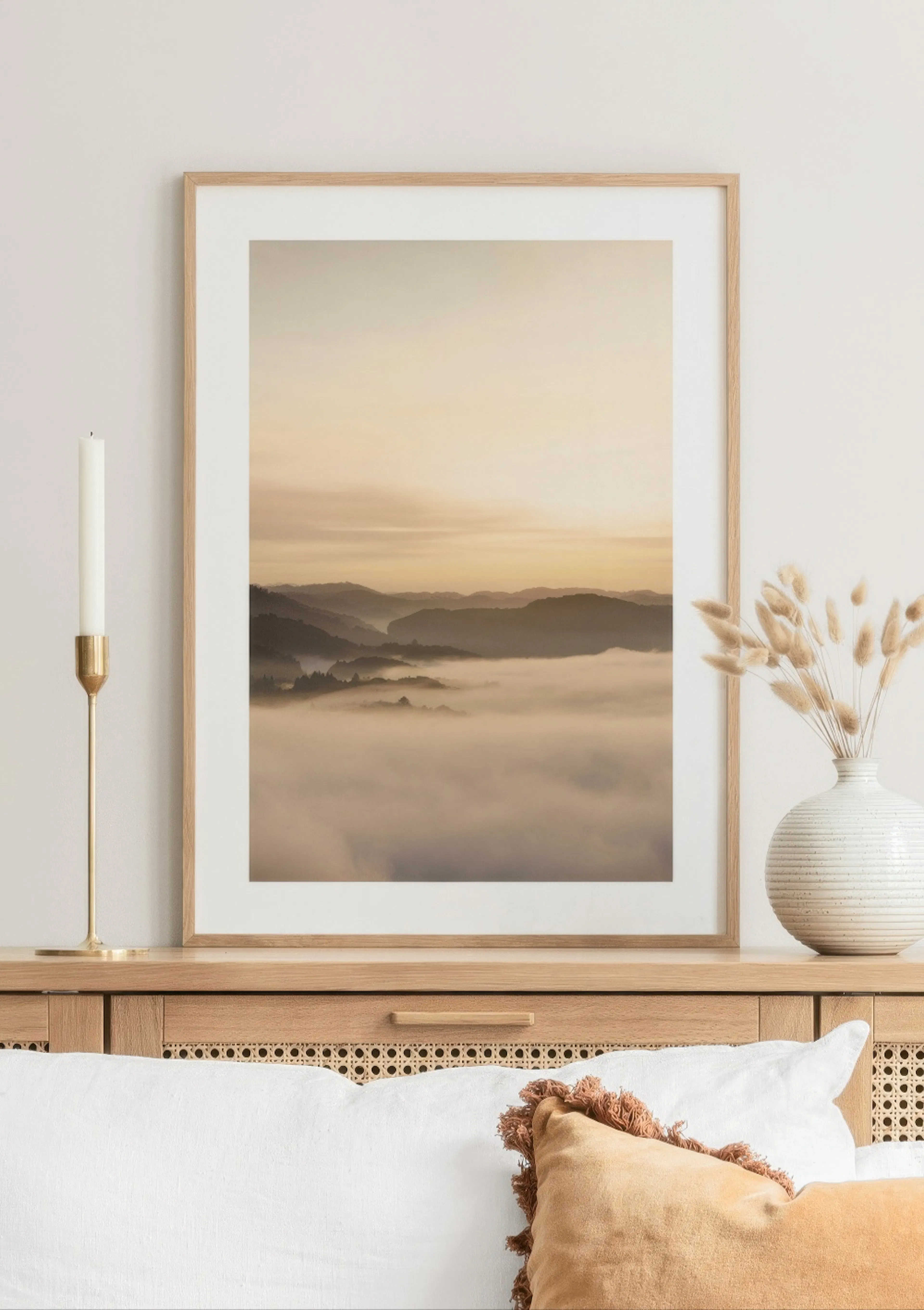 Un poster di un paesaggio montano nebbioso al tramonto, con nuvole dense che coprono le valli, appoggiato su una credenza in leg