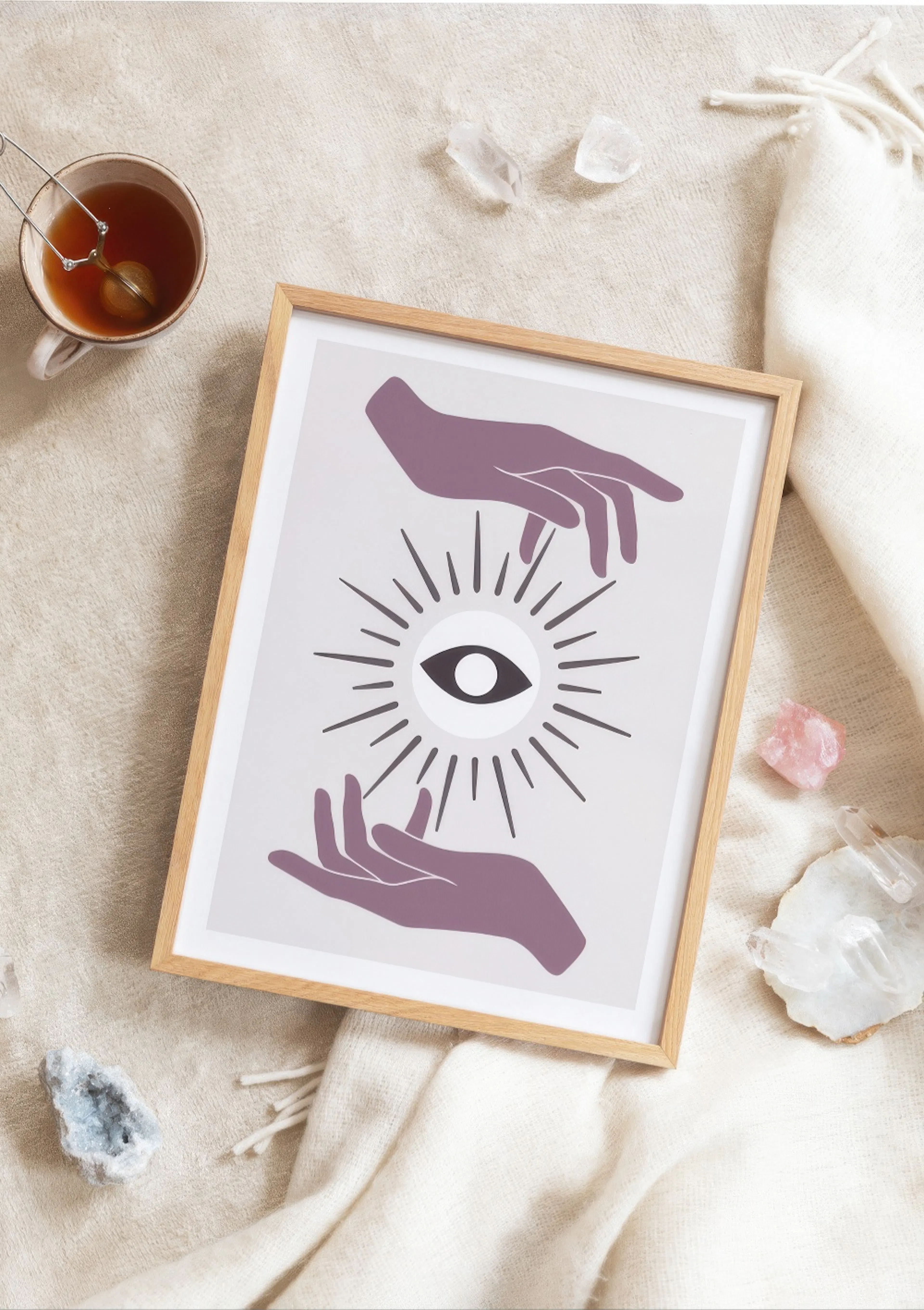 A poster with purple hands surrounding a central eye with radiating lines, displayed on a light blanket with tea and crystals.