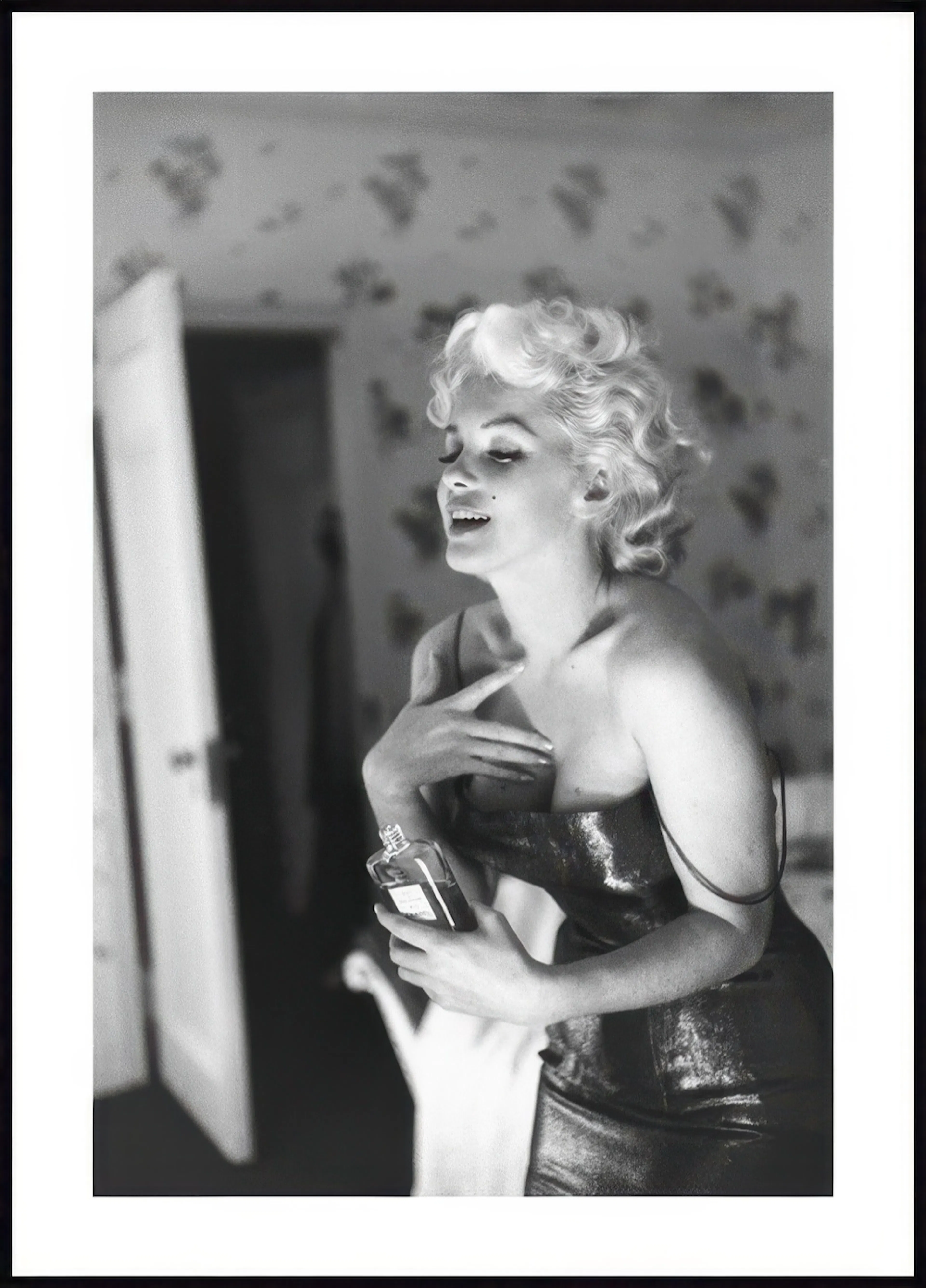 Póster en blanco y negro de Marilyn Monroe sonriendo, sosteniendo un frasco de perfume en un vestido brillante.