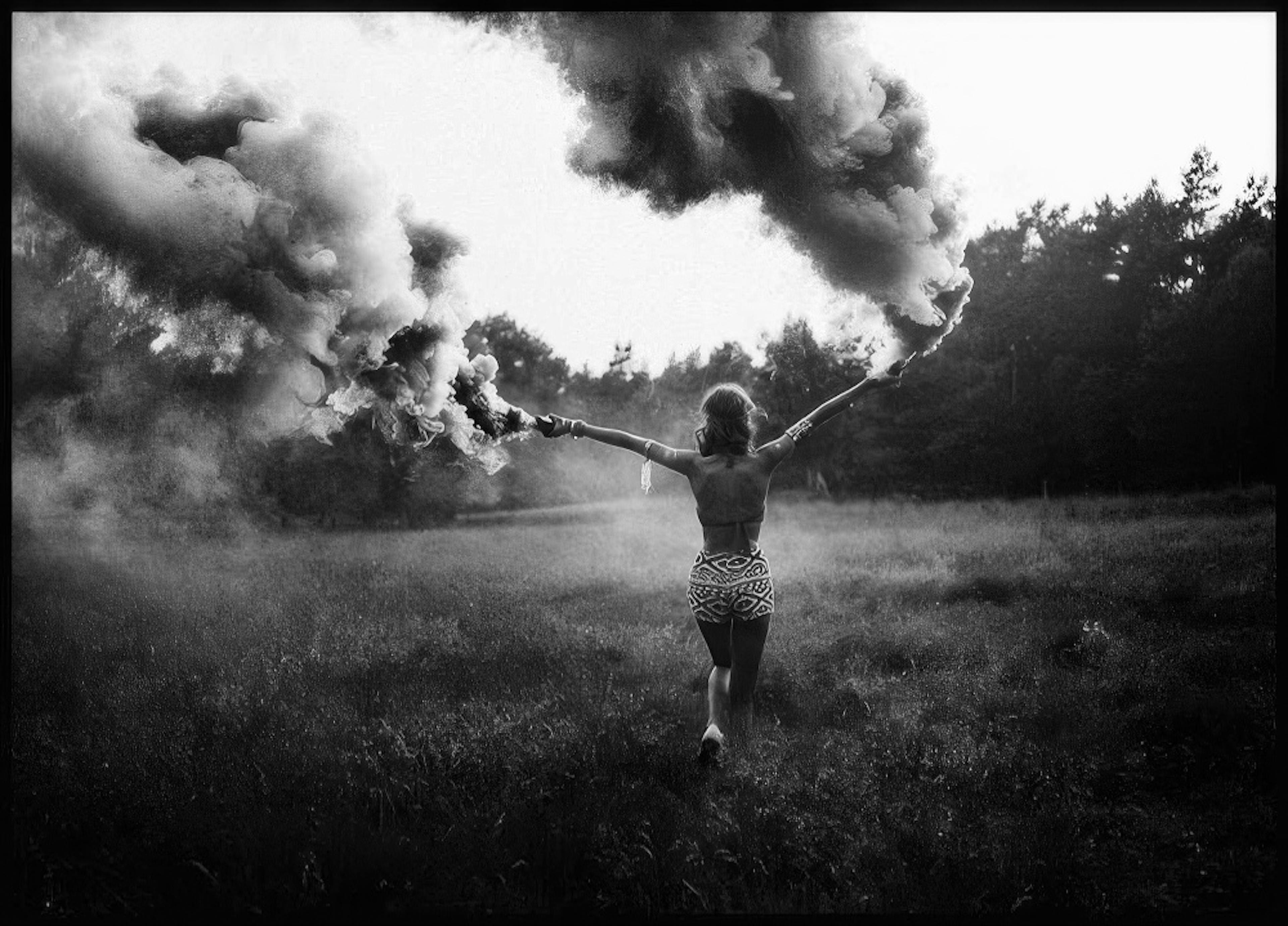 A monochrome poster of a woman running through a field with arms outstretched, holding smoke flares.