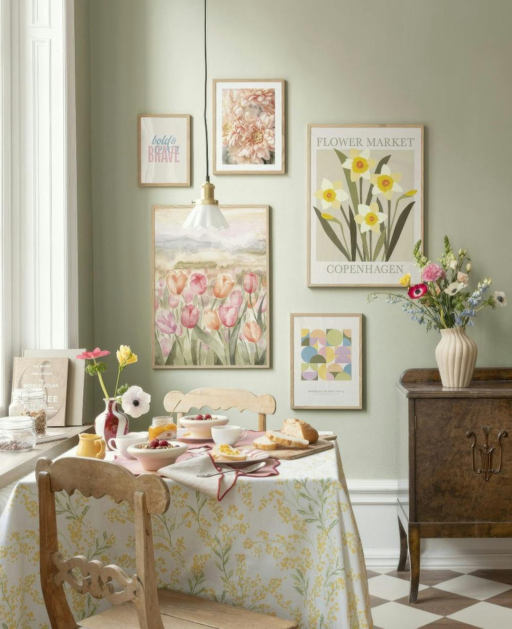 Un mural de cuadros con diseños florales, abstractos y tipográficos en una pared verde claro sobre una mesa de desayuno.