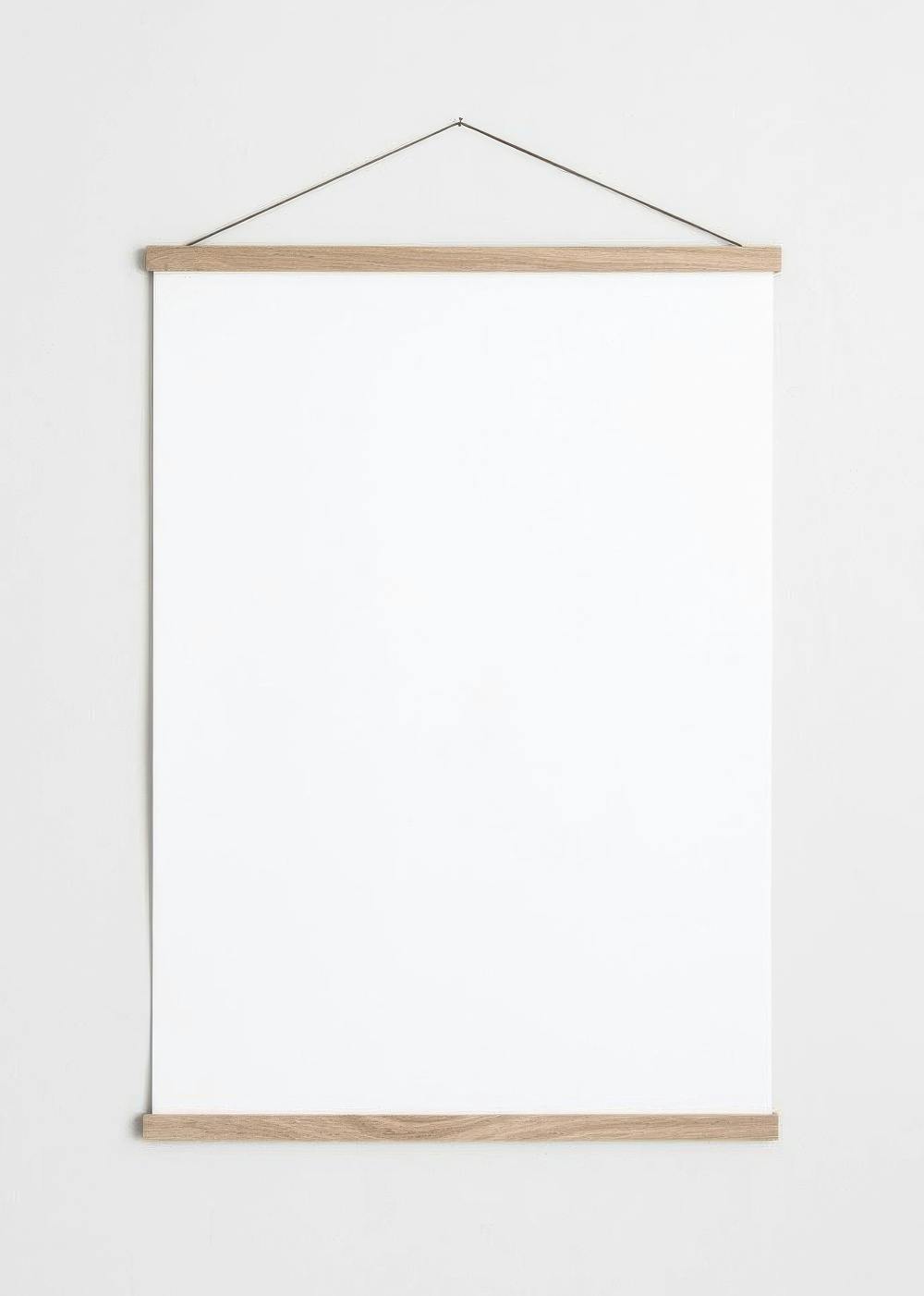 A blank white poster hanging on a light gray wall, held by light wooden magnetic poster hangers.
