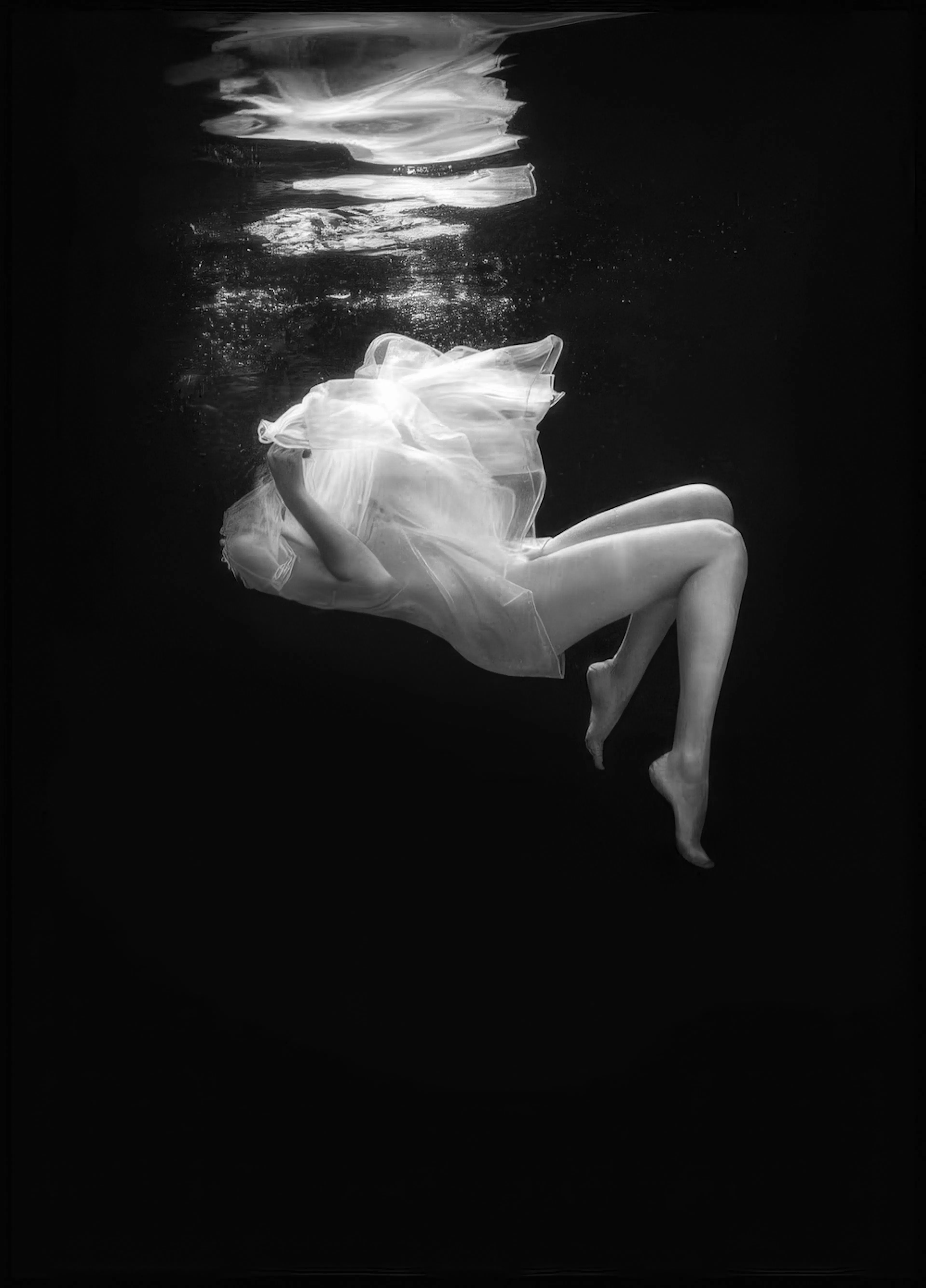 A poster of a woman floating in dark water, wearing a flowing white sheer dress, with her legs extended.