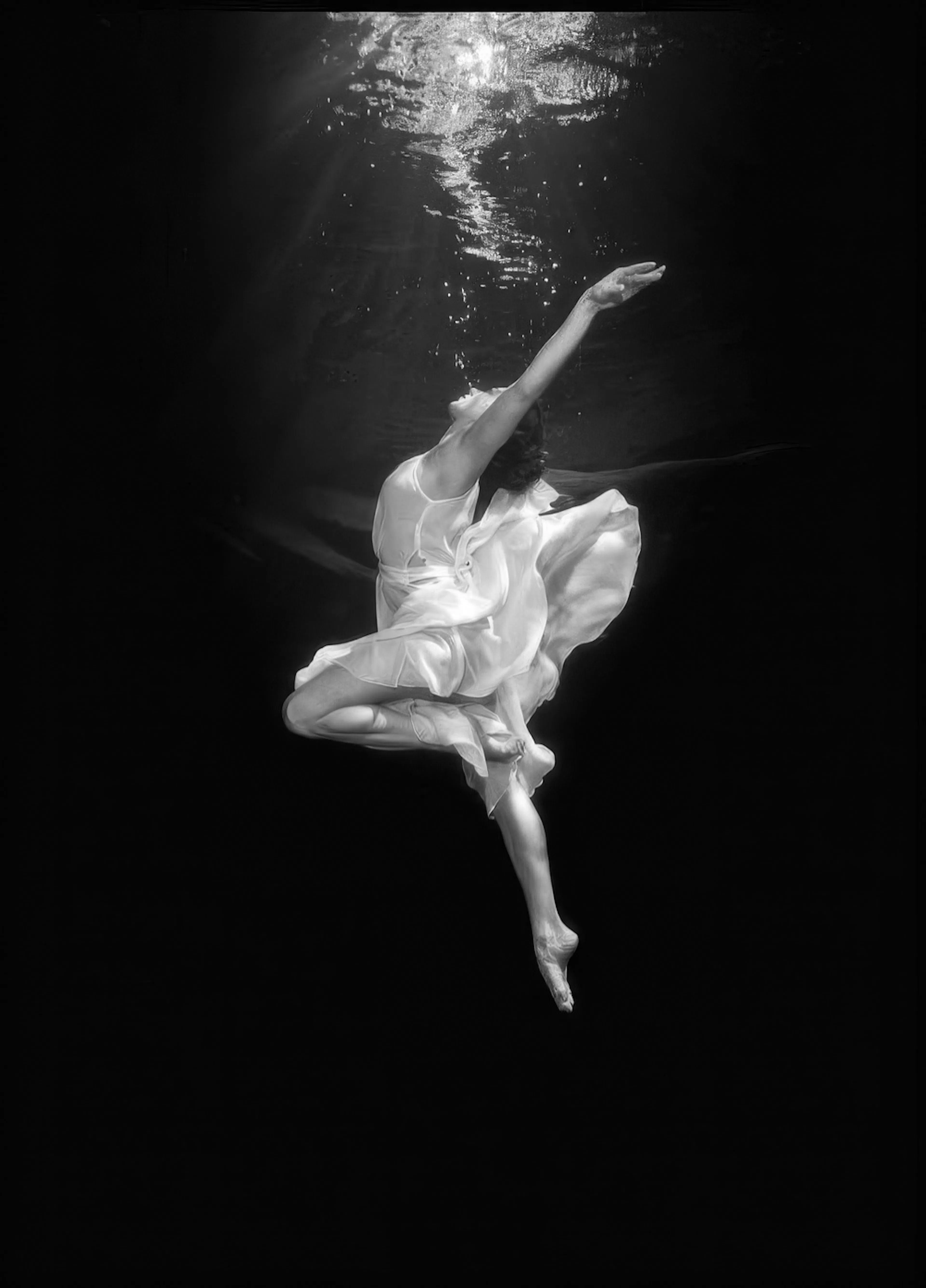 A poster of a woman gracefully suspended underwater, wearing a flowing white dress, in black and white.