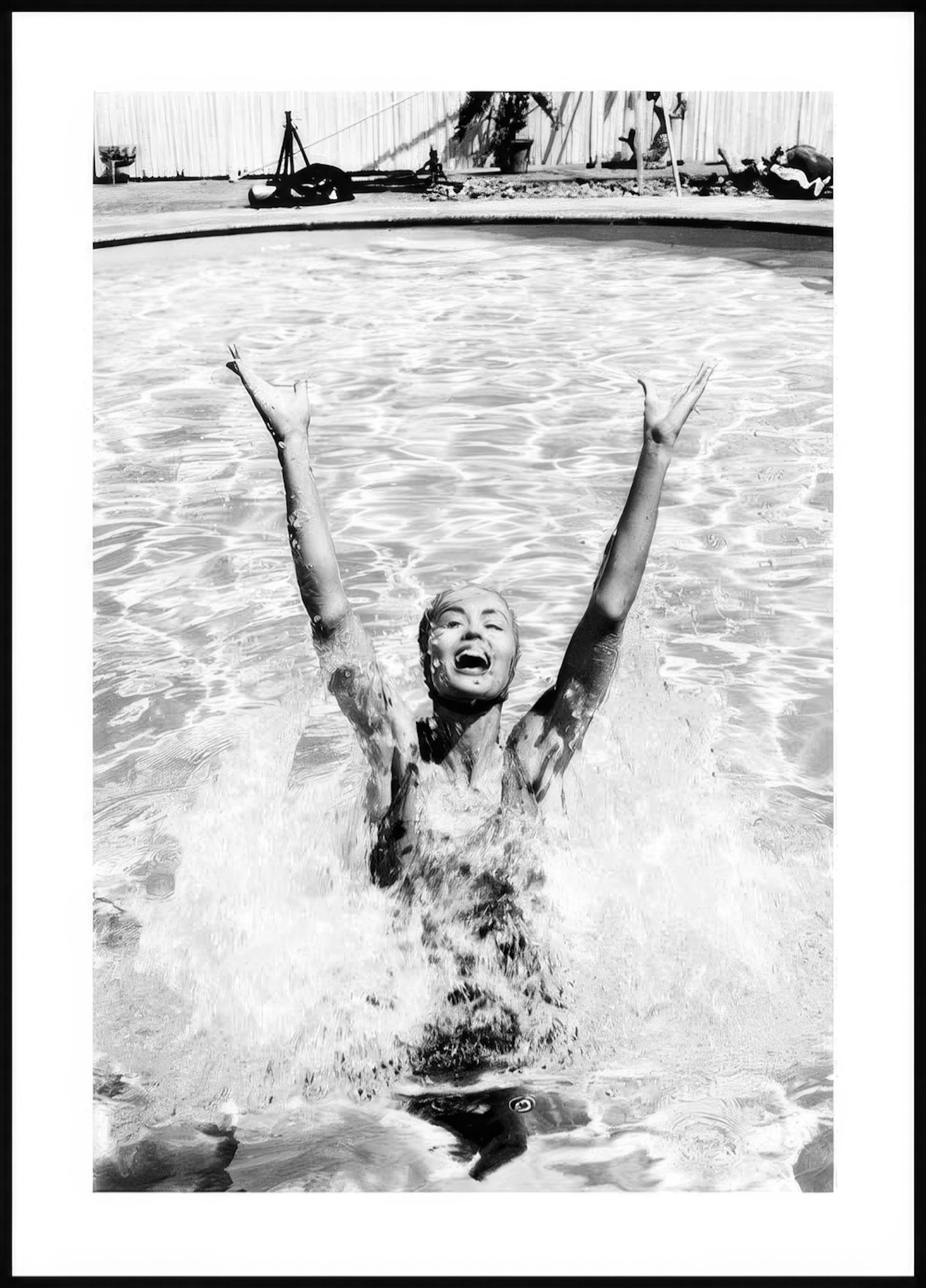 Mustavalkoinen juliste naisesta nousemassa vedestä, kädet ylhäällä ja vesi roiskuu iloisesti.