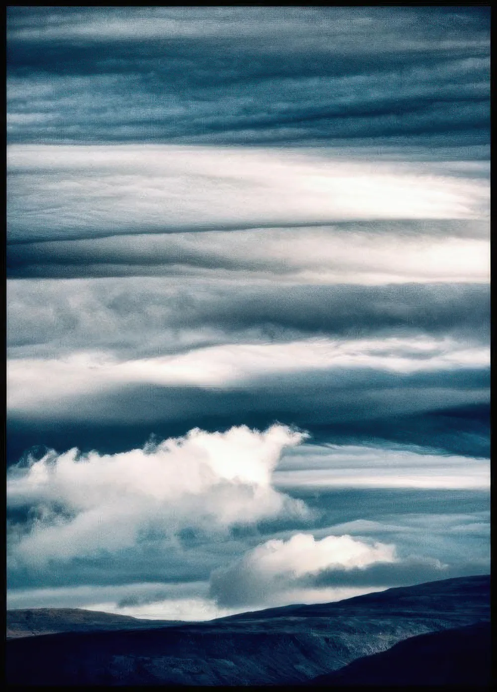Plakát zobrazuje vrstvené tmavě modré a šedobílé oblačné formace nad tmavou krajinou.