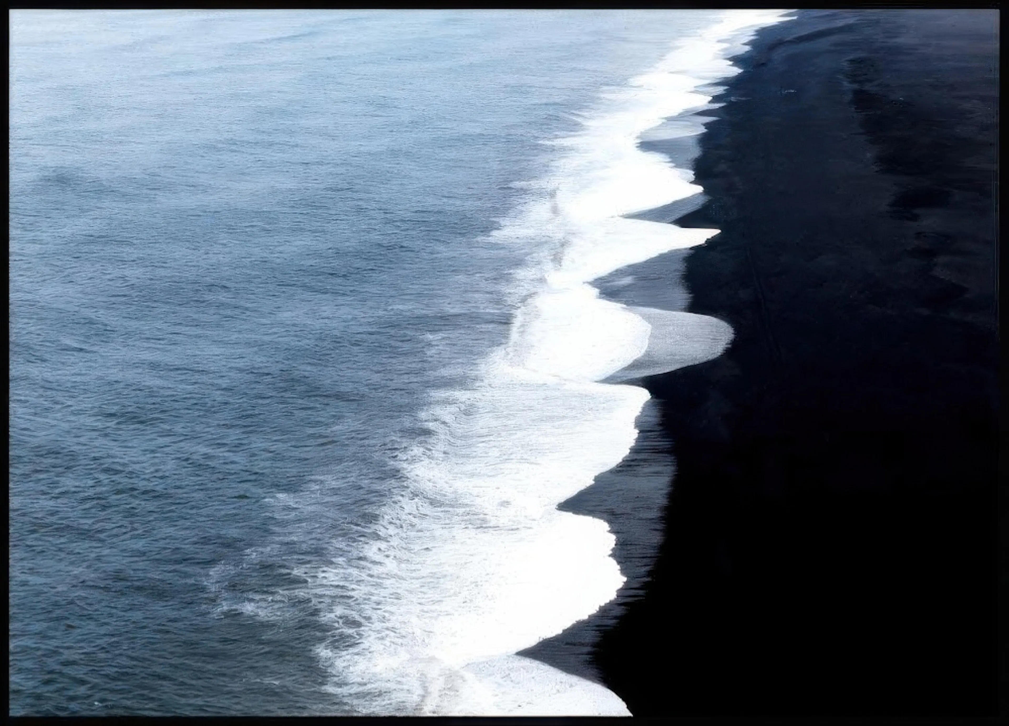 Plakát s pohledem shora na tmavý oceán a černou pláž s bílými vlnami.