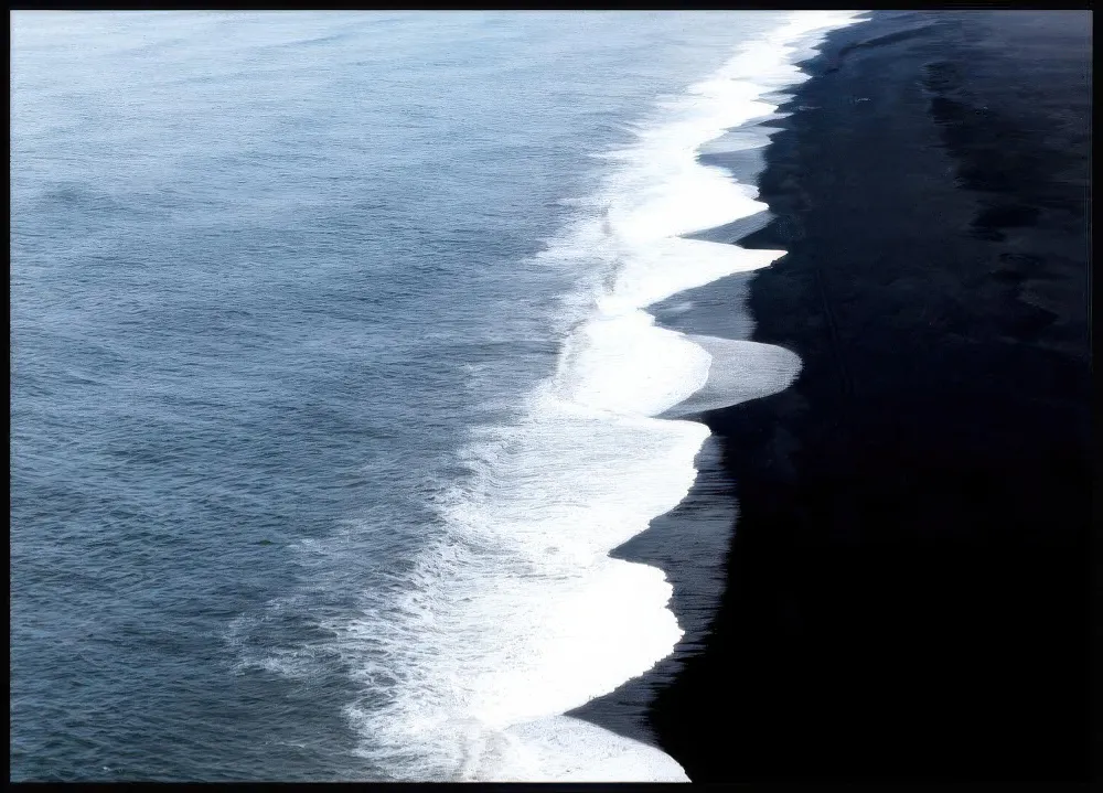 Plakát s pohledem shora na tmavý oceán a černou pláž s bílými vlnami.