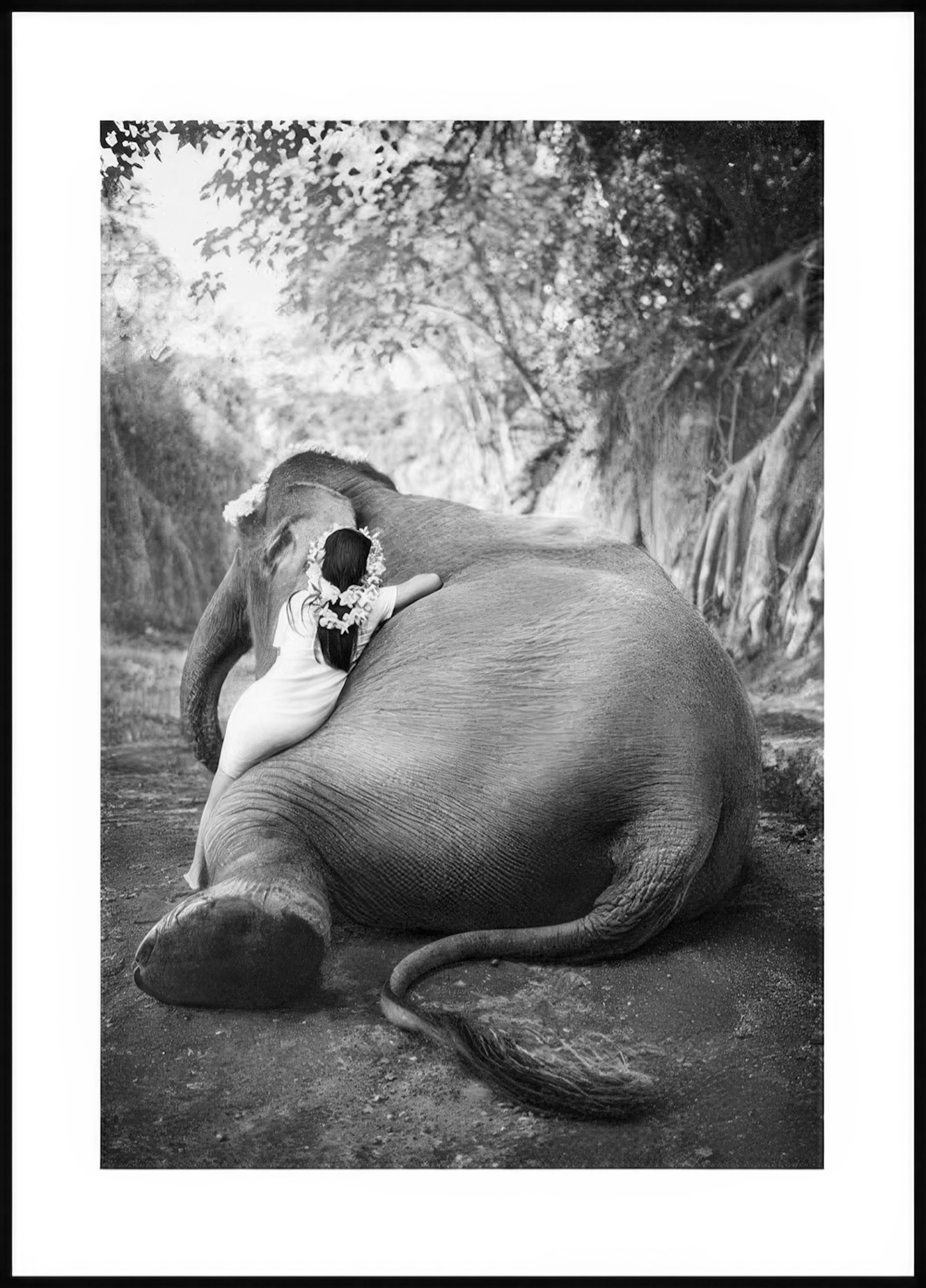 A black and white poster of a young girl with a flower garland embracing an elephant from behind.