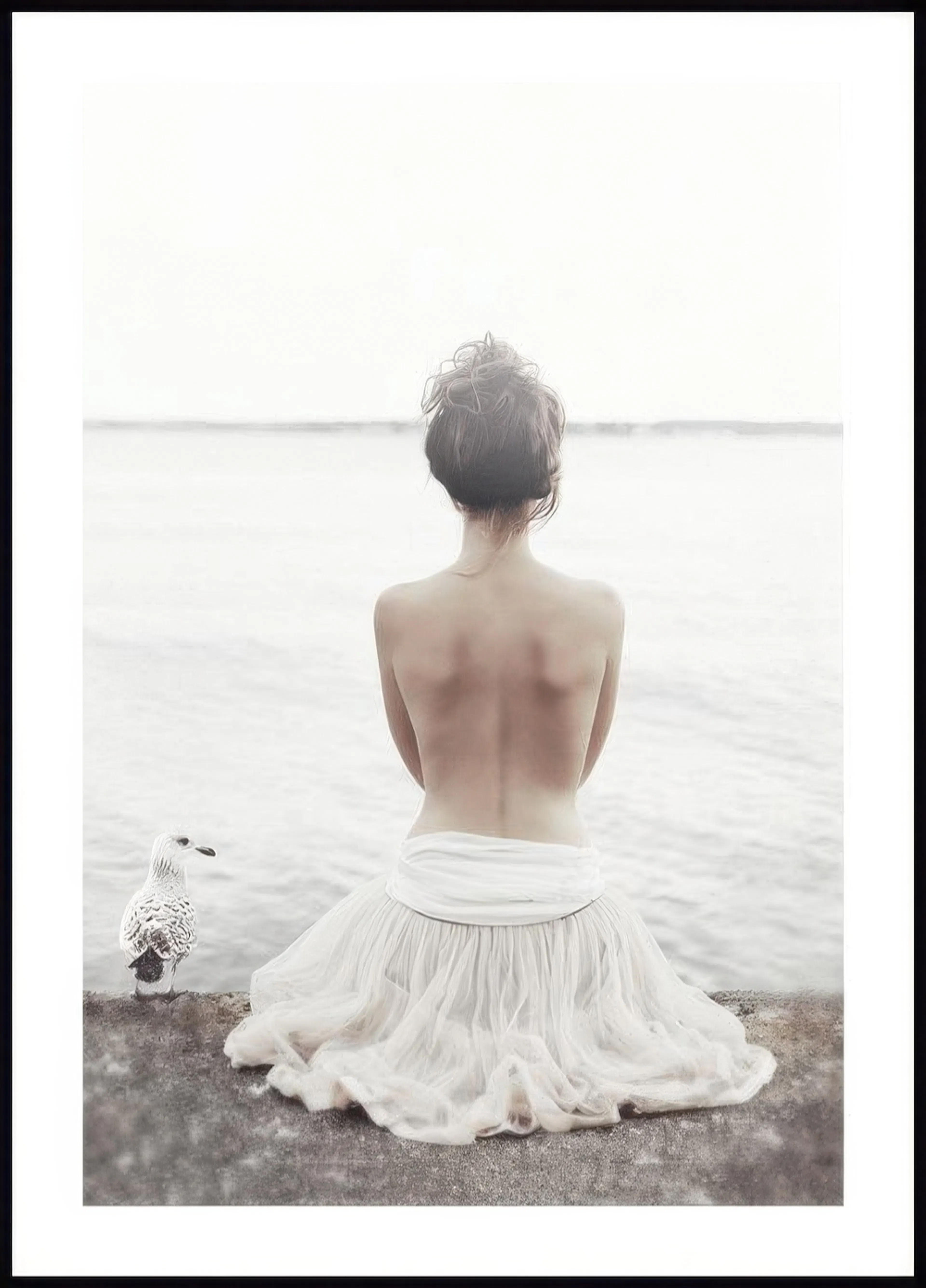 A poster featuring a woman in a white skirt with her back to the viewer, sitting by the water with a seagull beside her.