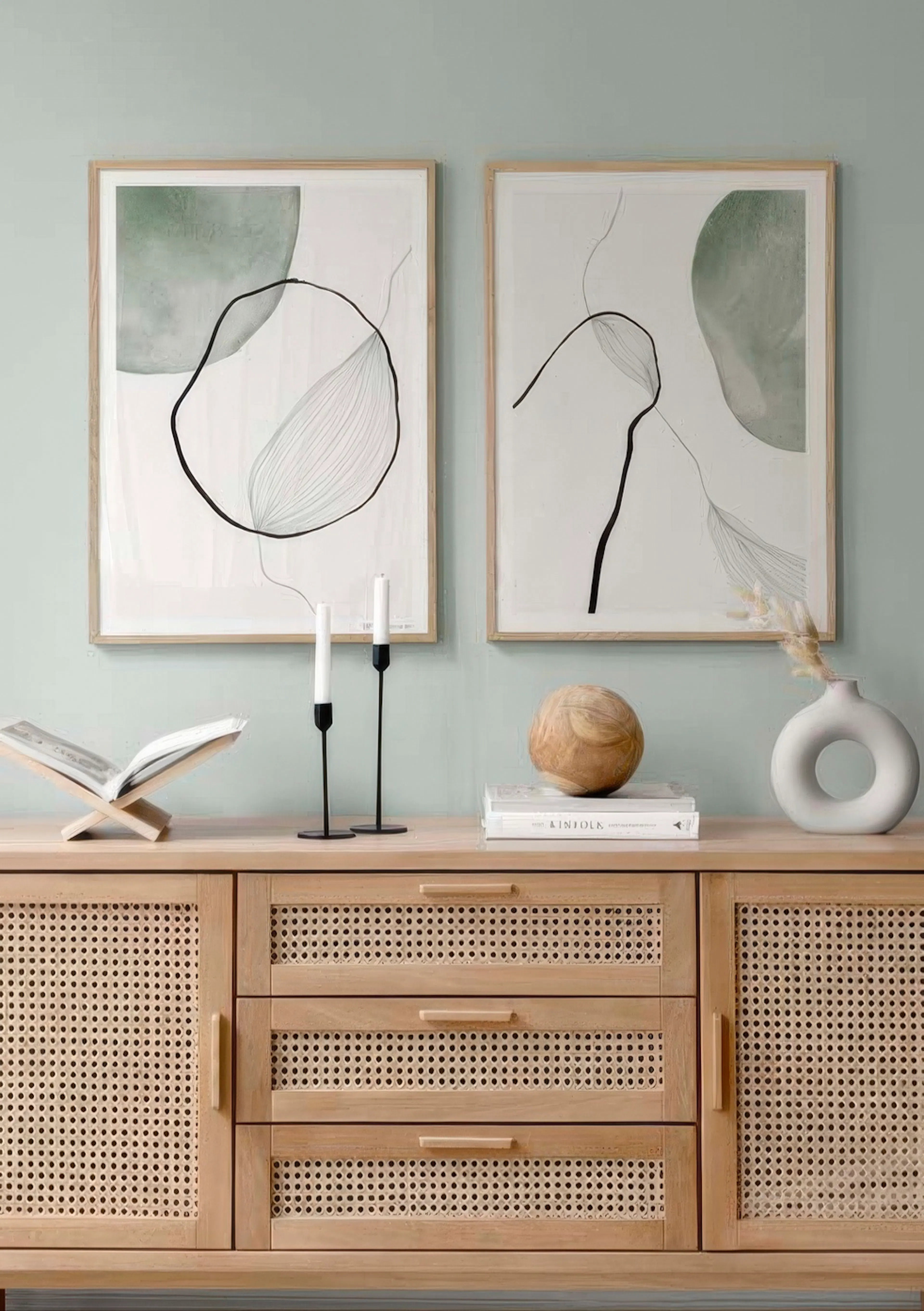 Paquetes de pósters abstractos con formas orgánicas verdes y líneas negras, sobre un mueble de madera.