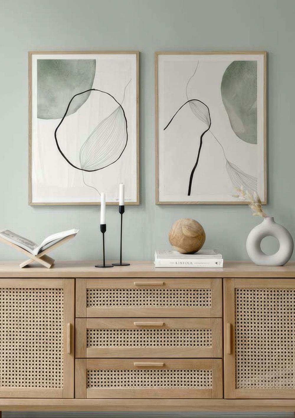 Twee postersets met abstracte groene vormen en zwarte organische lijnen, hangend boven een houten dressoir.